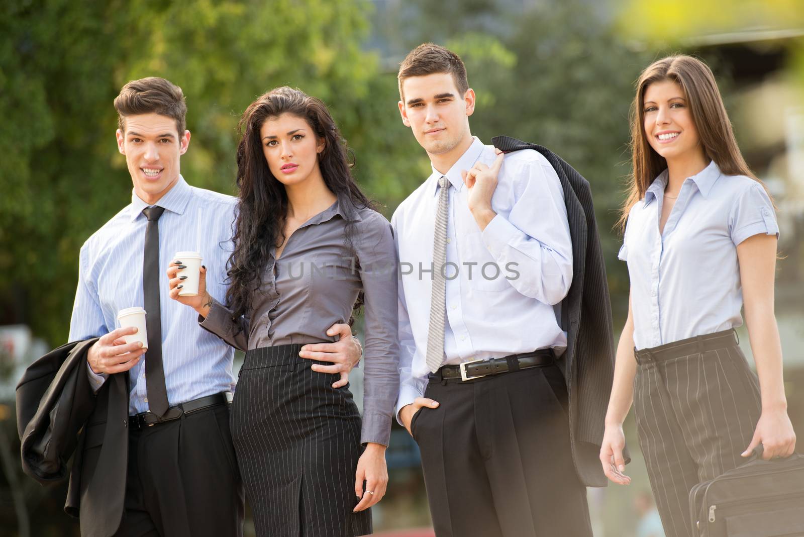Portrait of group of young successful business people dressed in suits,on coffee break standing outside, smiling looking at camera.