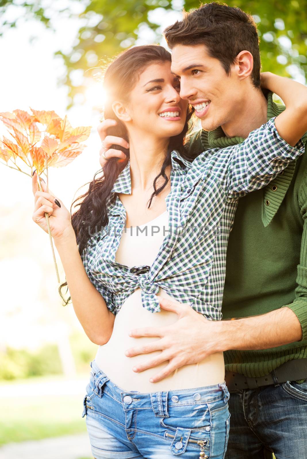 Young love couple in the park are embraced, a girl carries sprig of autumn leaves.