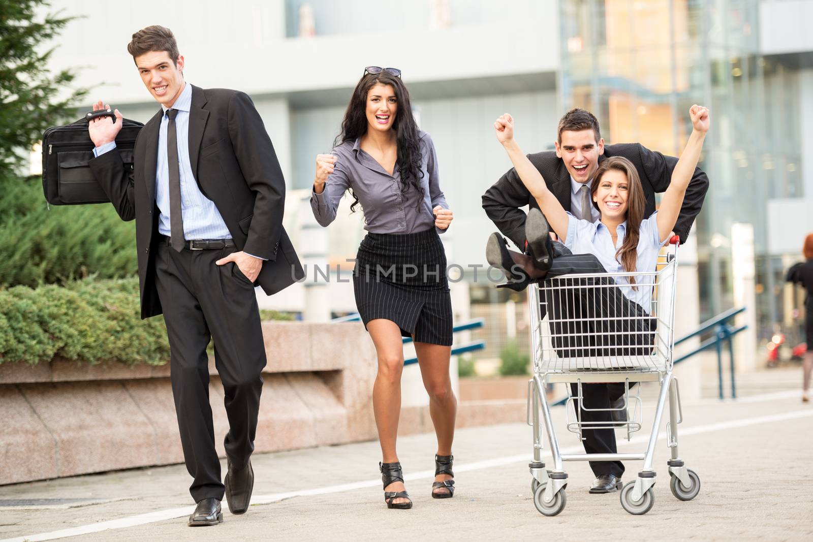 Group of young business people on the street near a supermarket in a hurry to sell, pushing their colleague in a shopping trolley.