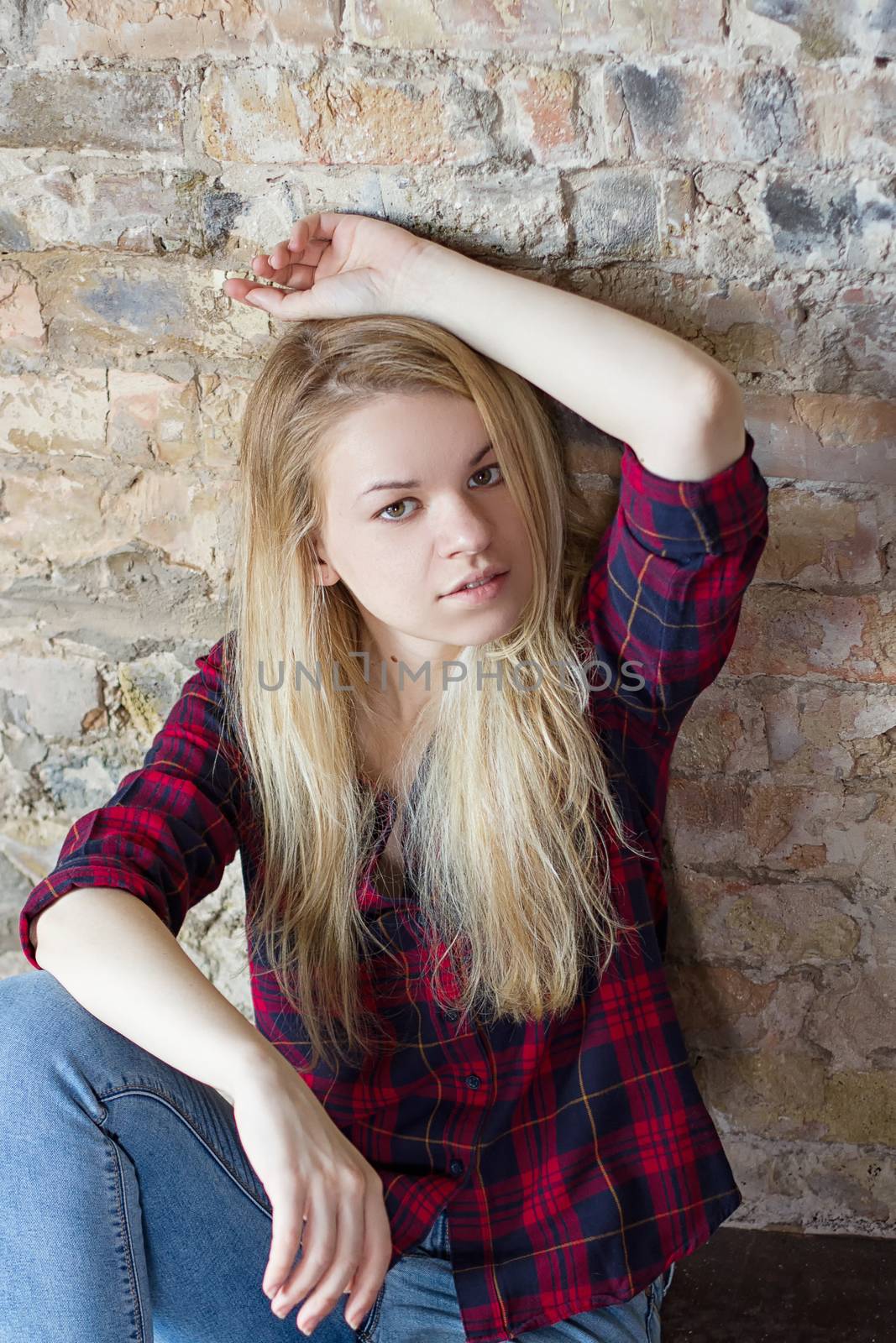 Front view of attractive white girl sitting on wooden floor against concrete wall