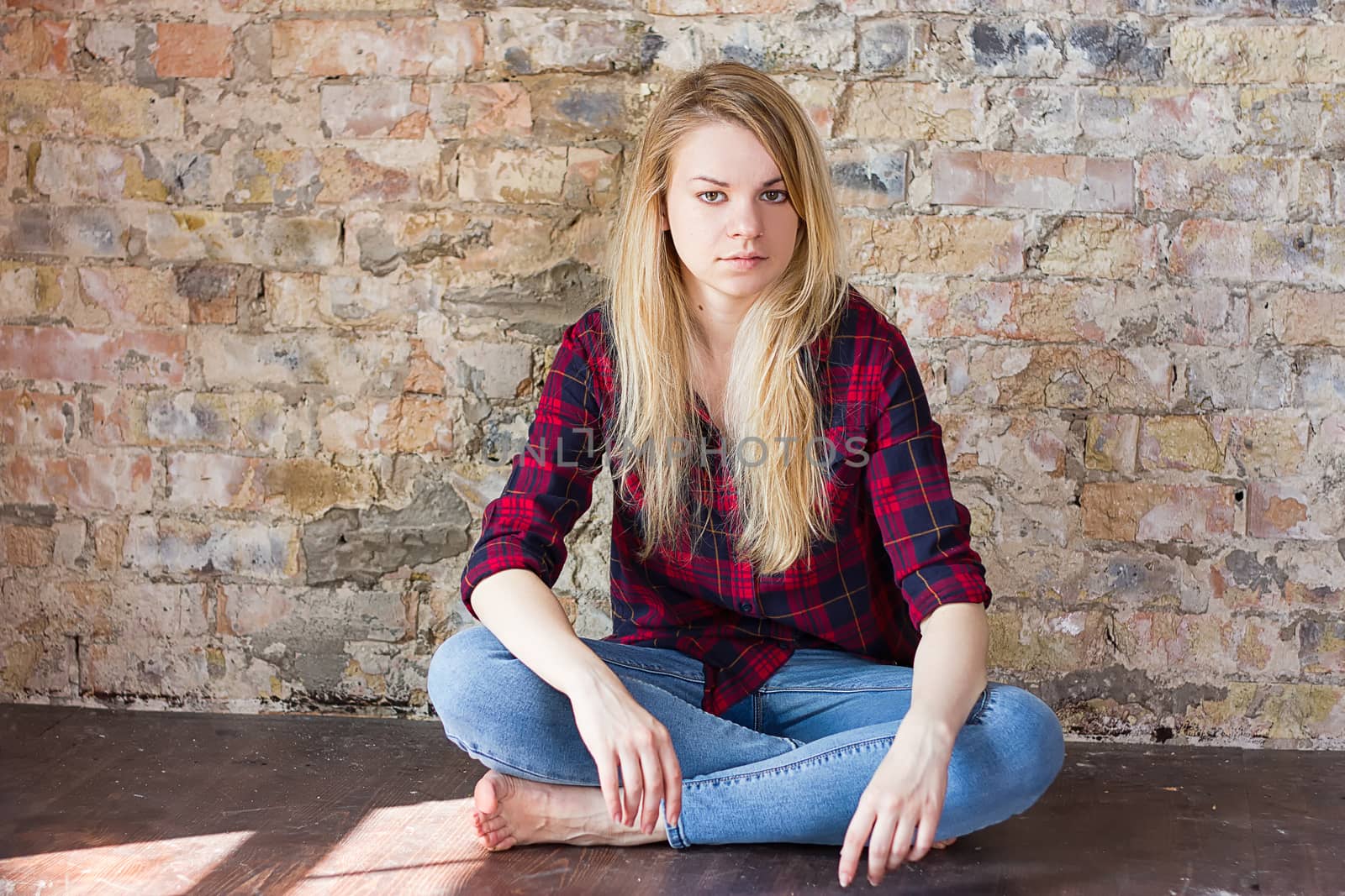 Front view of attractive white girl sitting on wooden floor against concrete wall