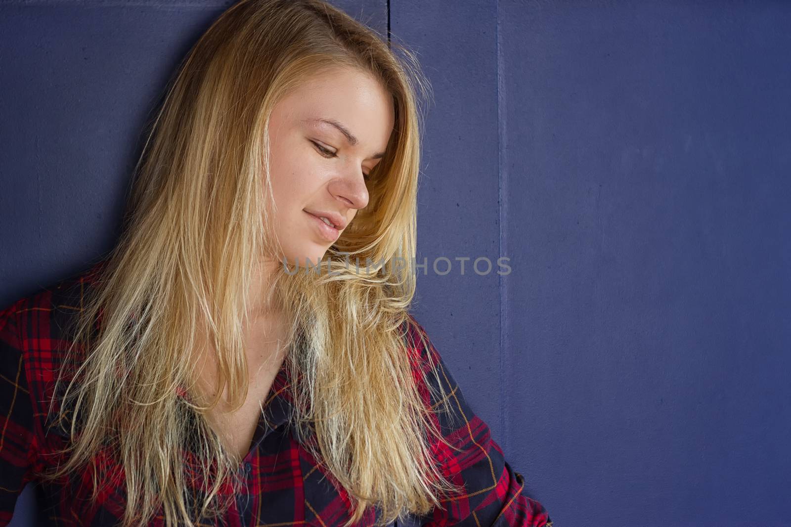 Portrait of a young beautiful girl with closed eyes, a beautiful smile. Posing on a background of an blue wall.