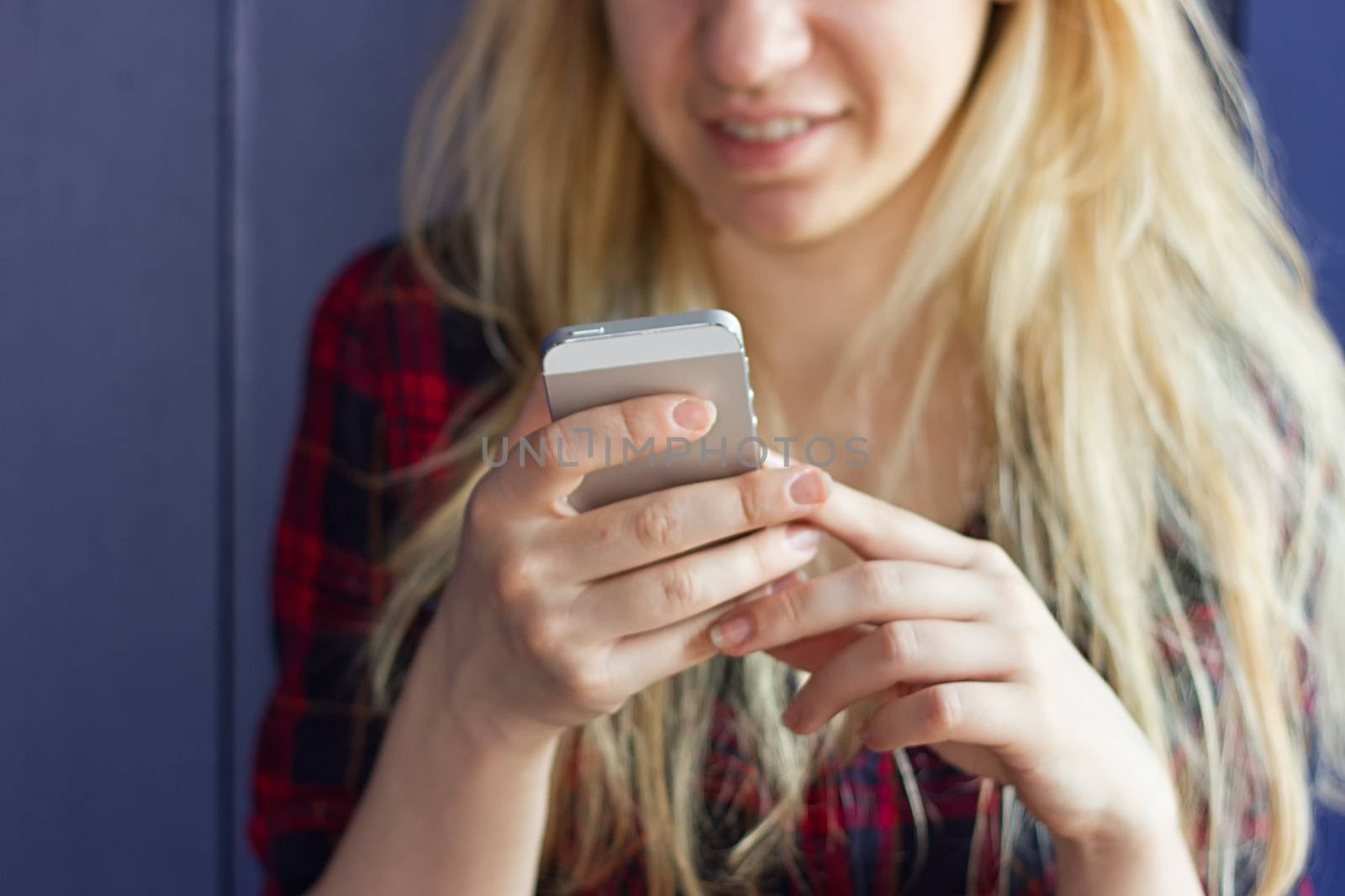 Cute Girl playing with her Phone on a blue Wall