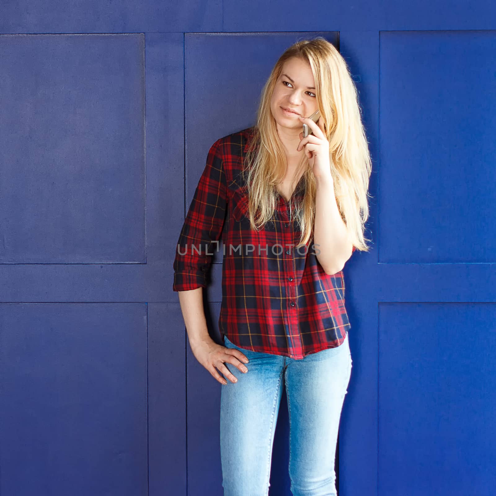 Pretty Woman Calling Someone Through Mobile Phone While Smiling at the Camera Against Blue Wall Background