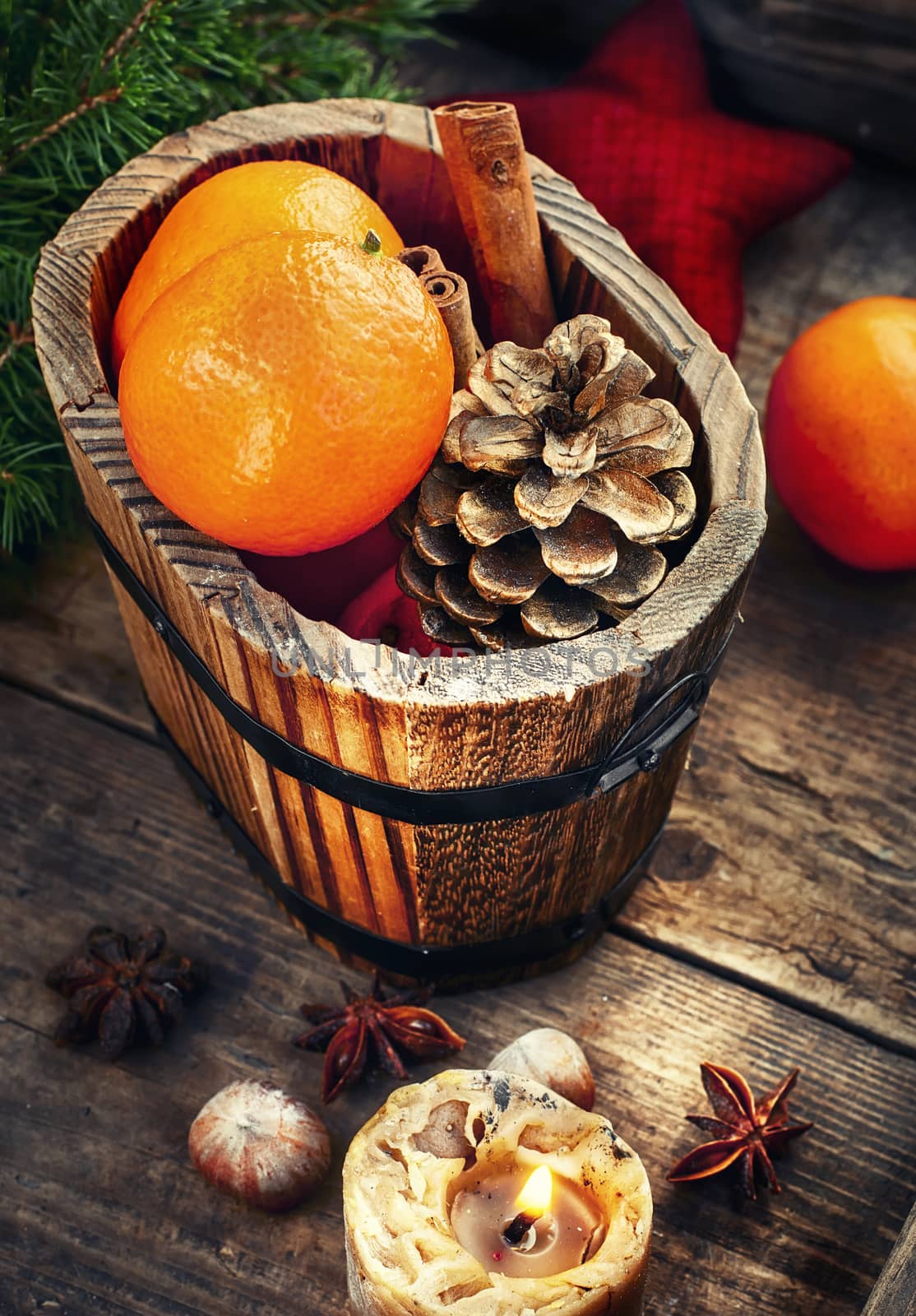 Wooden bucket with tangerines and pine cone and a burning Christmas candle