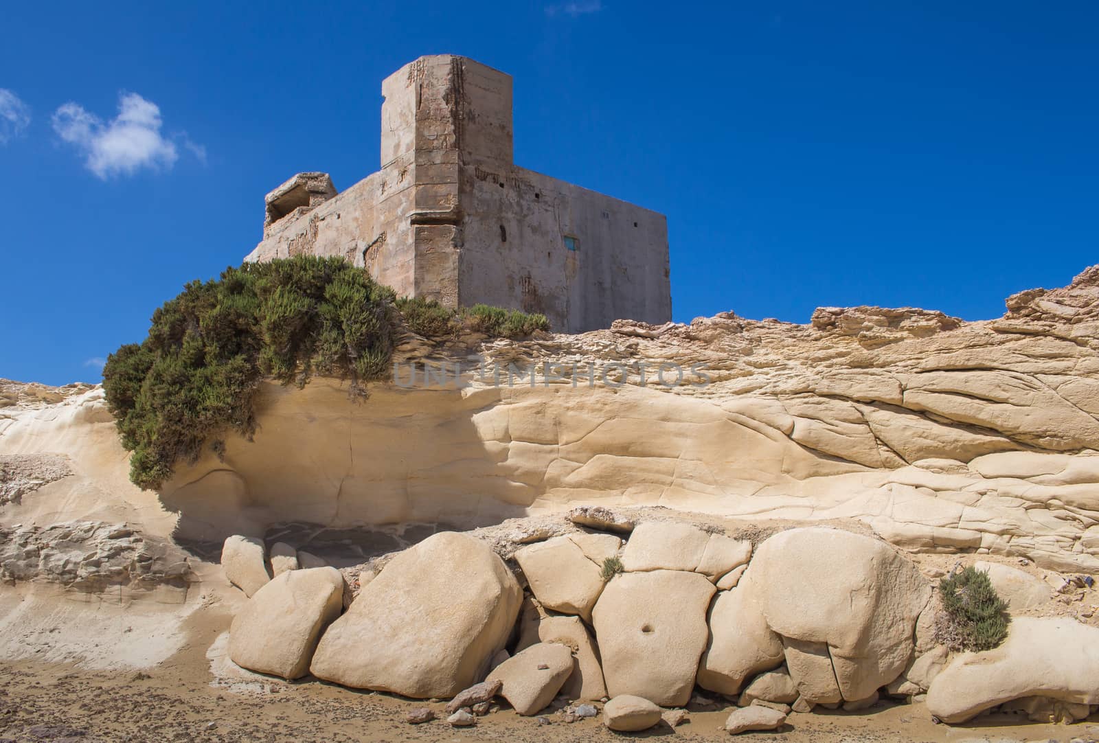 Sand color of the rocks on the coast of Mediterranean sea, city Marsaskala, island Malta. Building on the top of the hill. Bright blue sky, few white clouds.