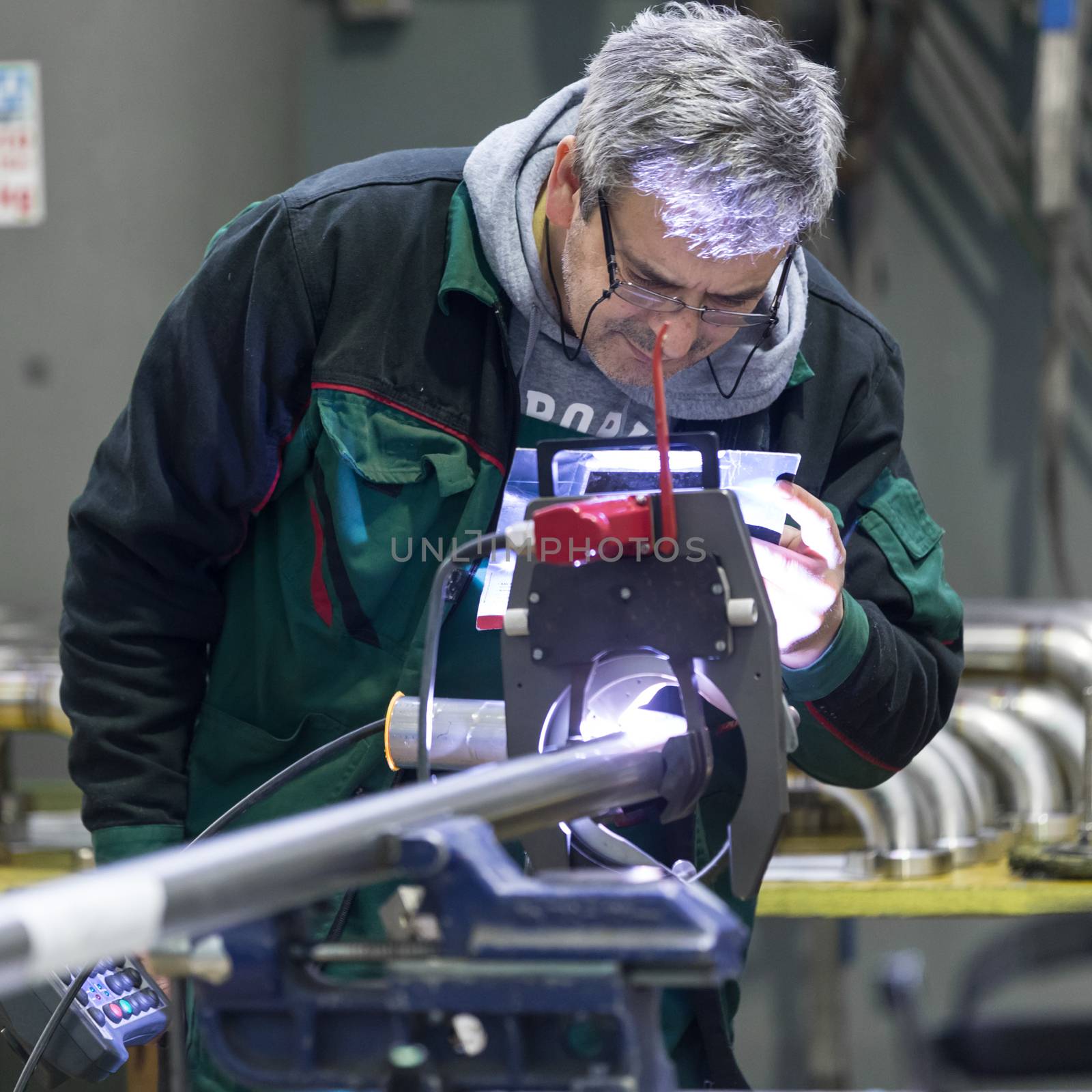 Industrial operator setting  computer controlled process of orbital welding machine in  stainless steel pipes manufacturing workshop. Square composition.