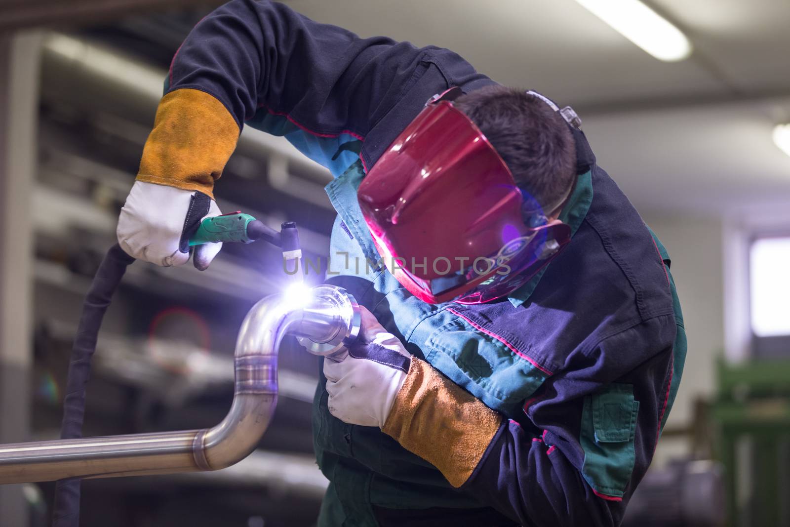 Industrial worker with protective mask welding inox elements in steel structures manufacture workshop.