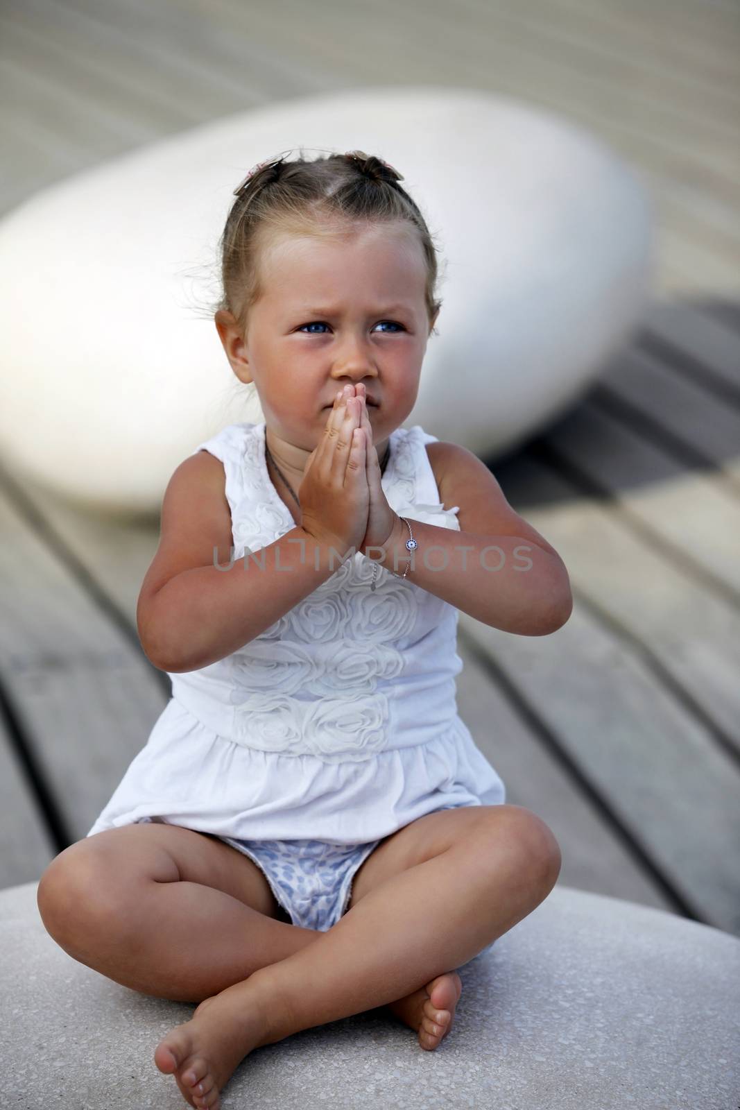 Adorable little girl doing yoga sitting on the big stone