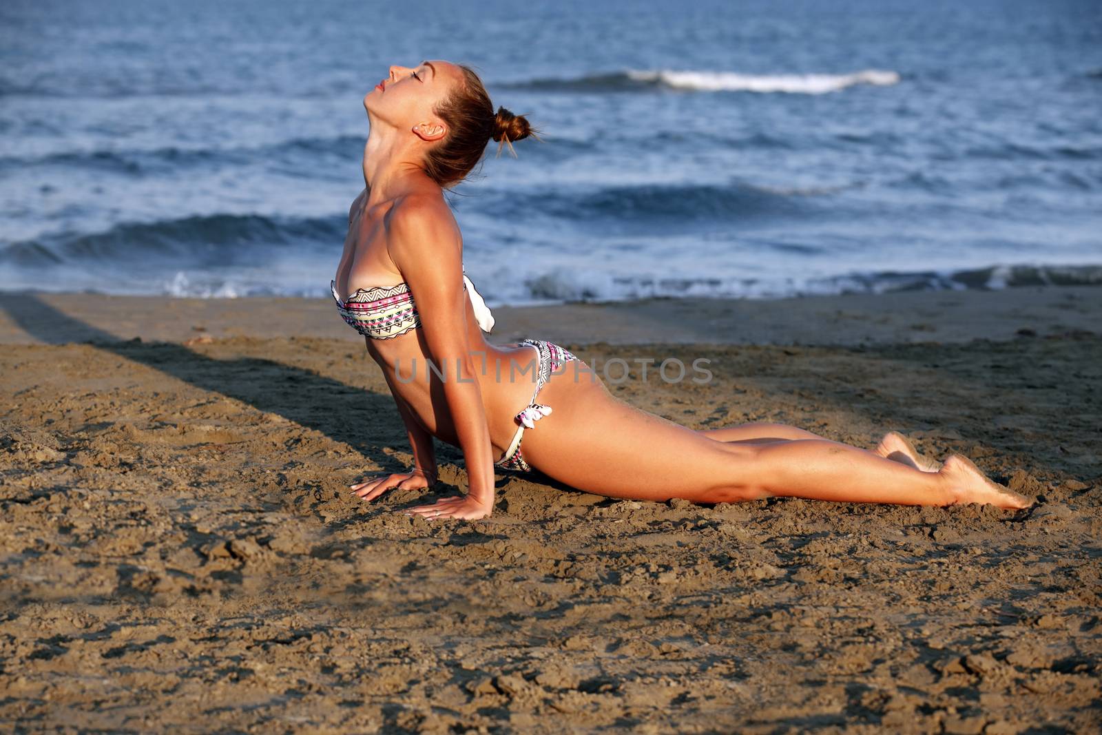 Young woman practicing yoga on the sea beach at sunset