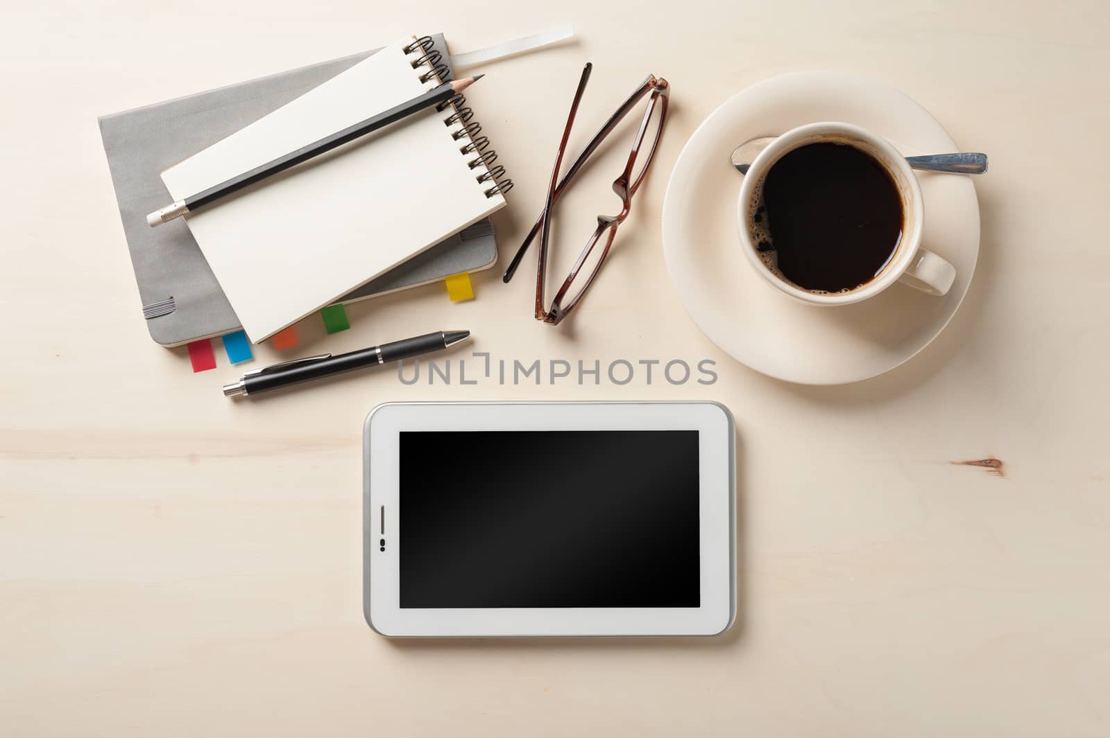 Small tablet pc, notebooks, pen, glasses, and coffee cup on wood table in cafe at morning time