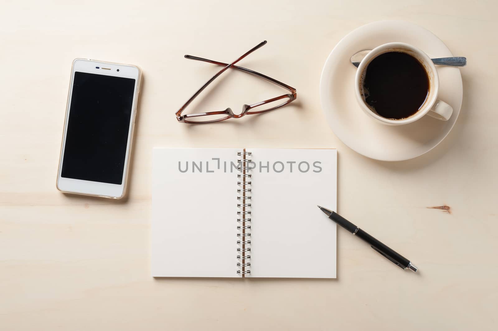 Opened notebook with blank area, pen, smart phone, and coffee cup on wood table in morning time