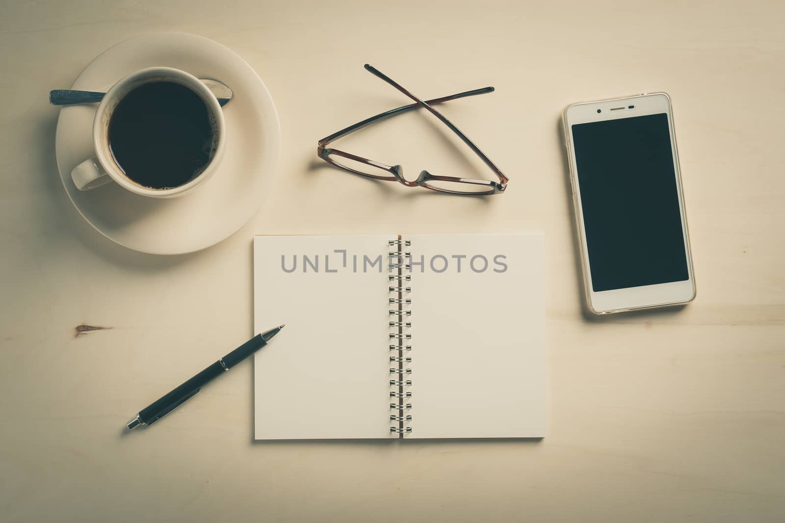 Opened notebook with blank area, pen, smart phone, and coffee cup on wood table in morning time with vintage filter effect