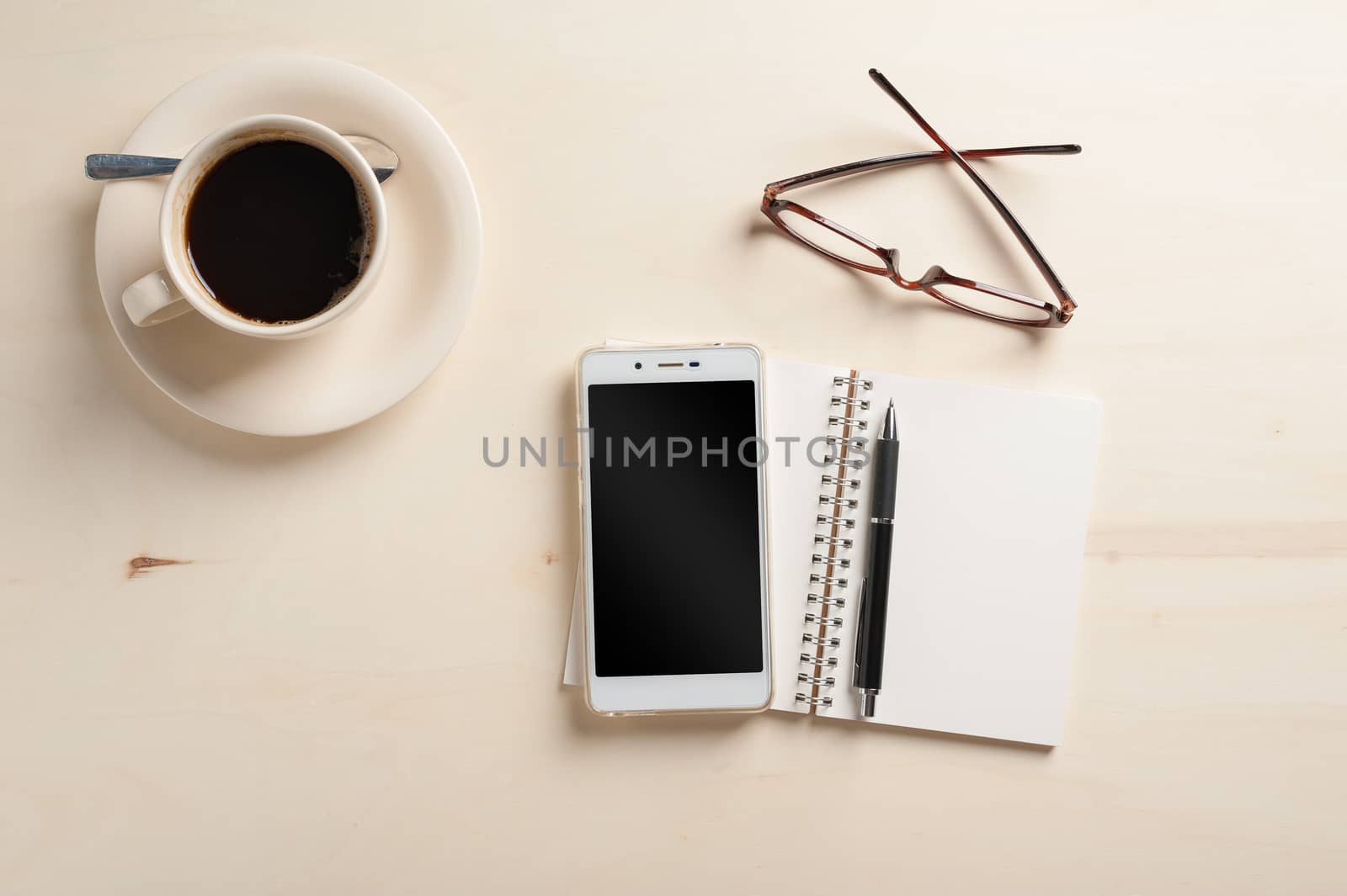 Opened notebook with blank area, pen, smart phone, and coffee cup on wood table in morning time
