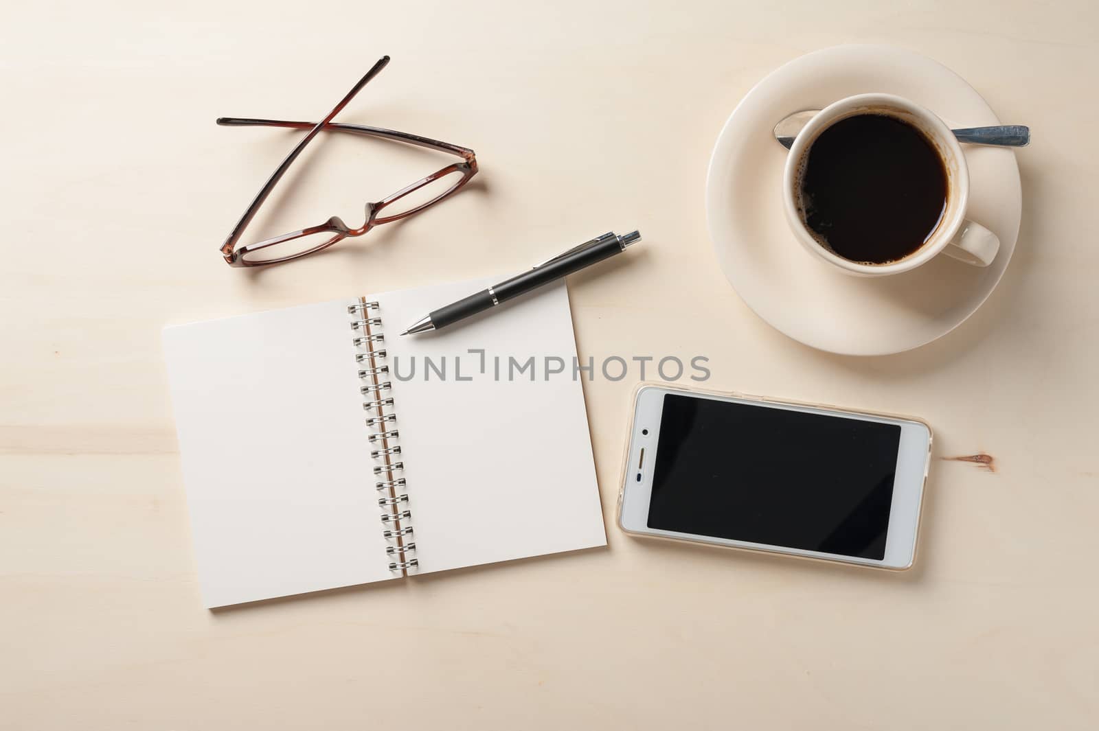 Opened notebook with blank area, pen, smart phone, and coffee cup on wood table in morning time