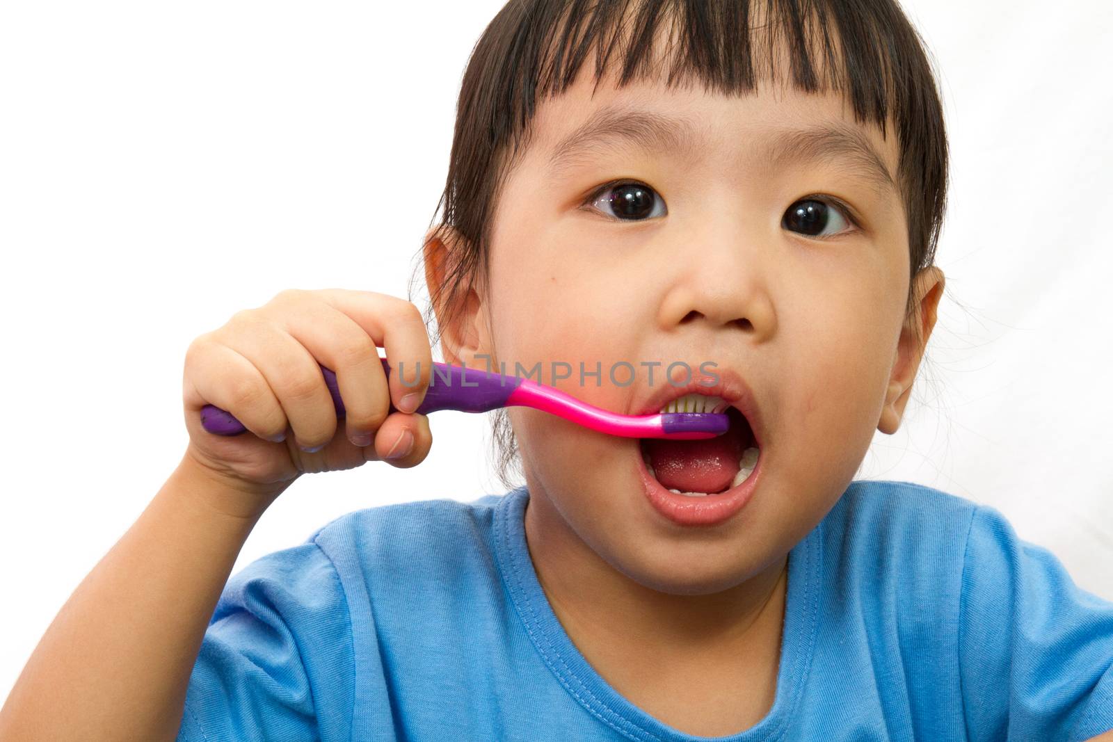 Chinese little girl brushing teeth in plain white isolated background.
