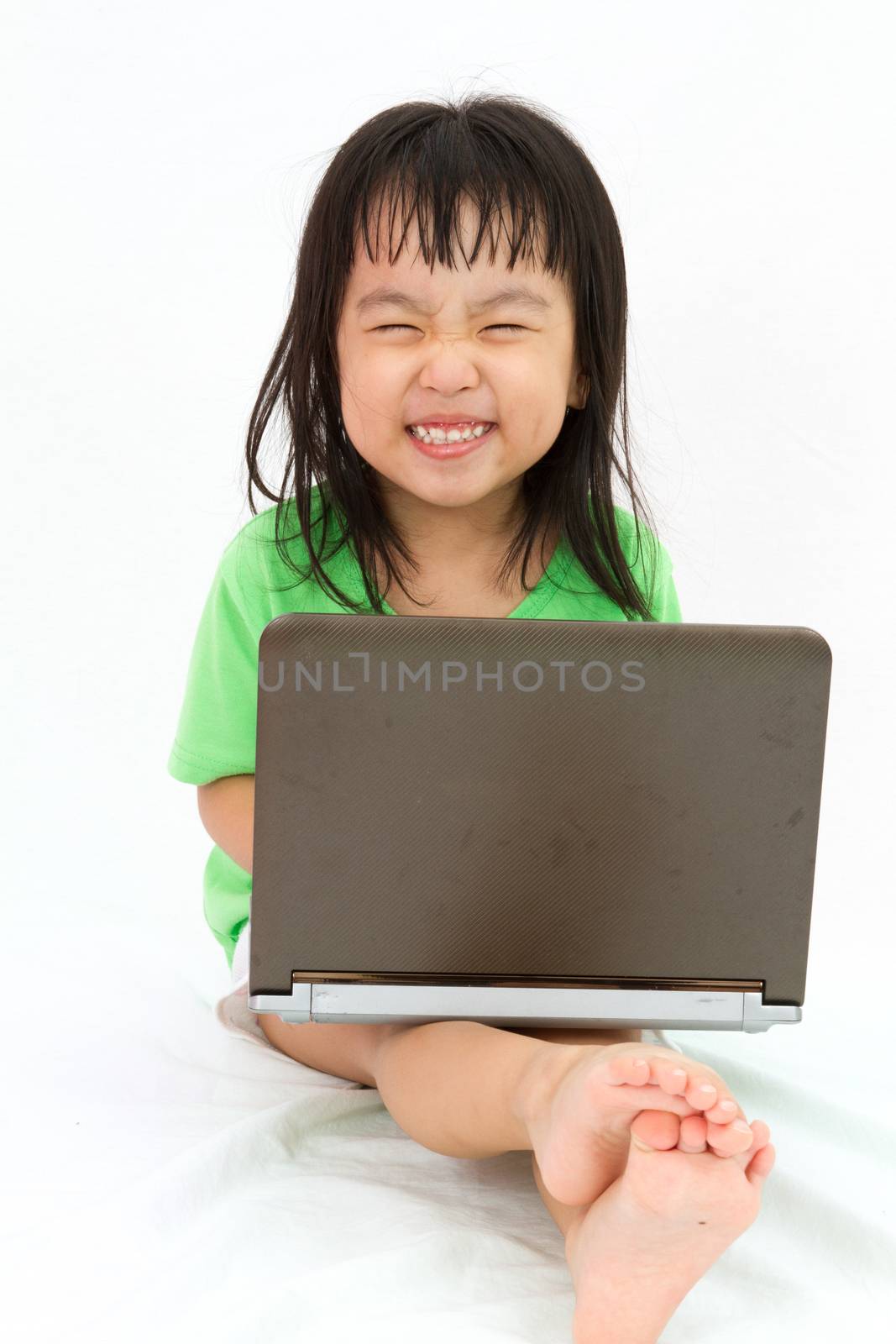 Chinese little girl sitting on floor with laptop in plain isolated white background.