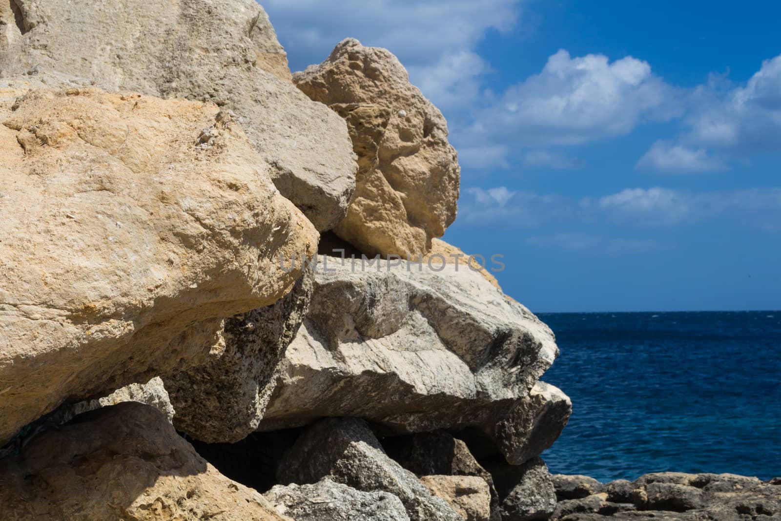 Sand color of the rocks. Coast of mediterranean island Malta, city Marsaskala. Horizon of a blue water. Bright blue sky with some clouds.