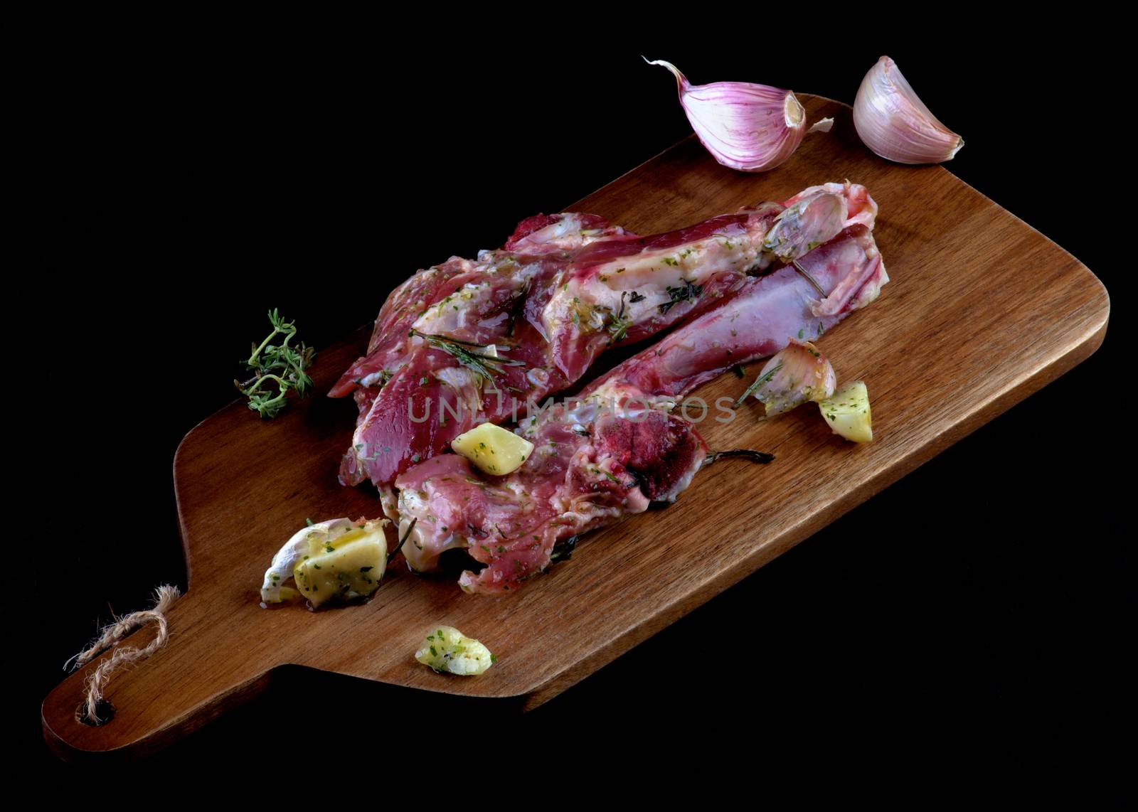 Delicious Raw Lamb Ribs in Marinade of Herbs and Spices with Rosemary and Garlic on Wooden Cutting Board closeup on Dark background