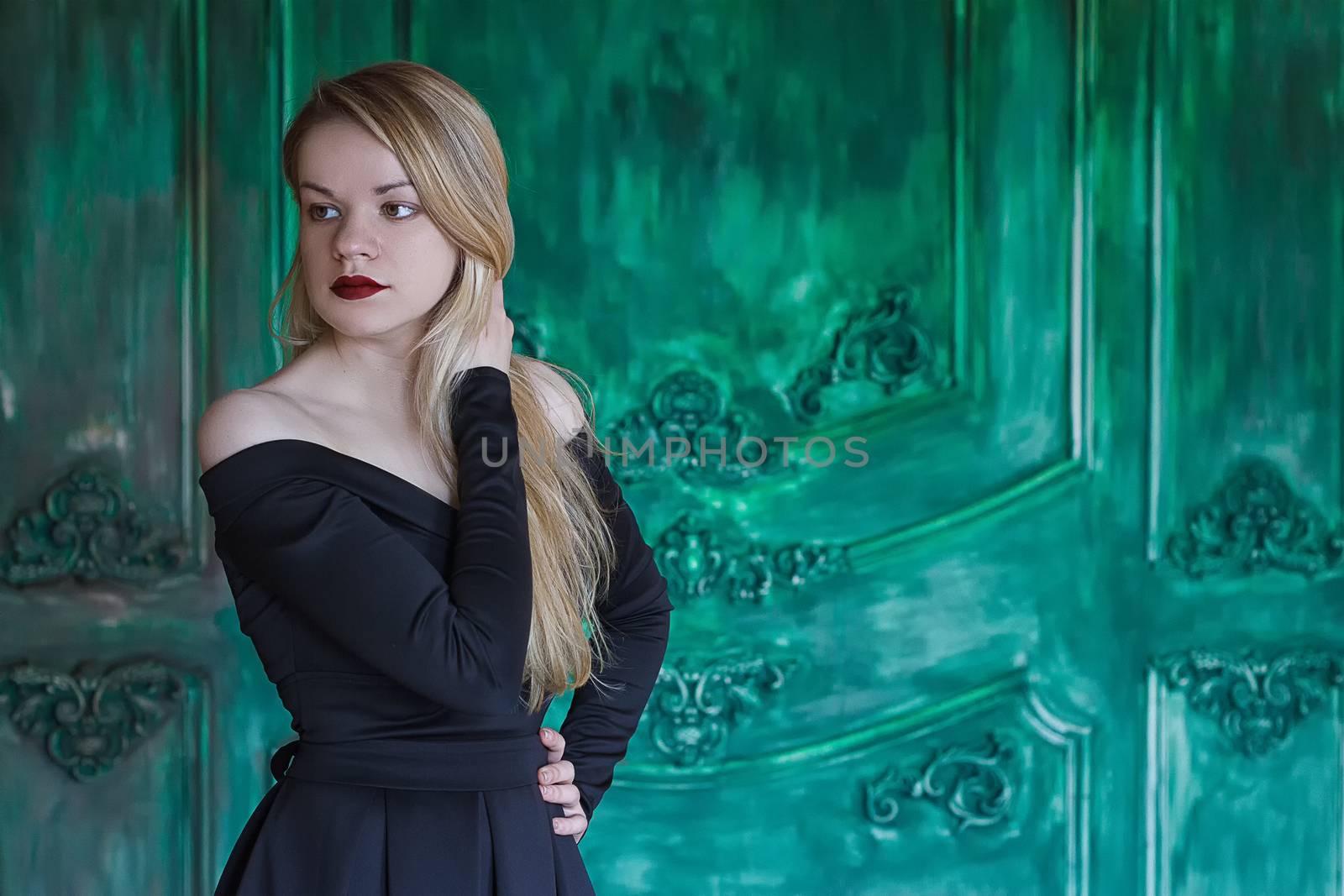 Elegant blonde in a black dress near grunge wall green