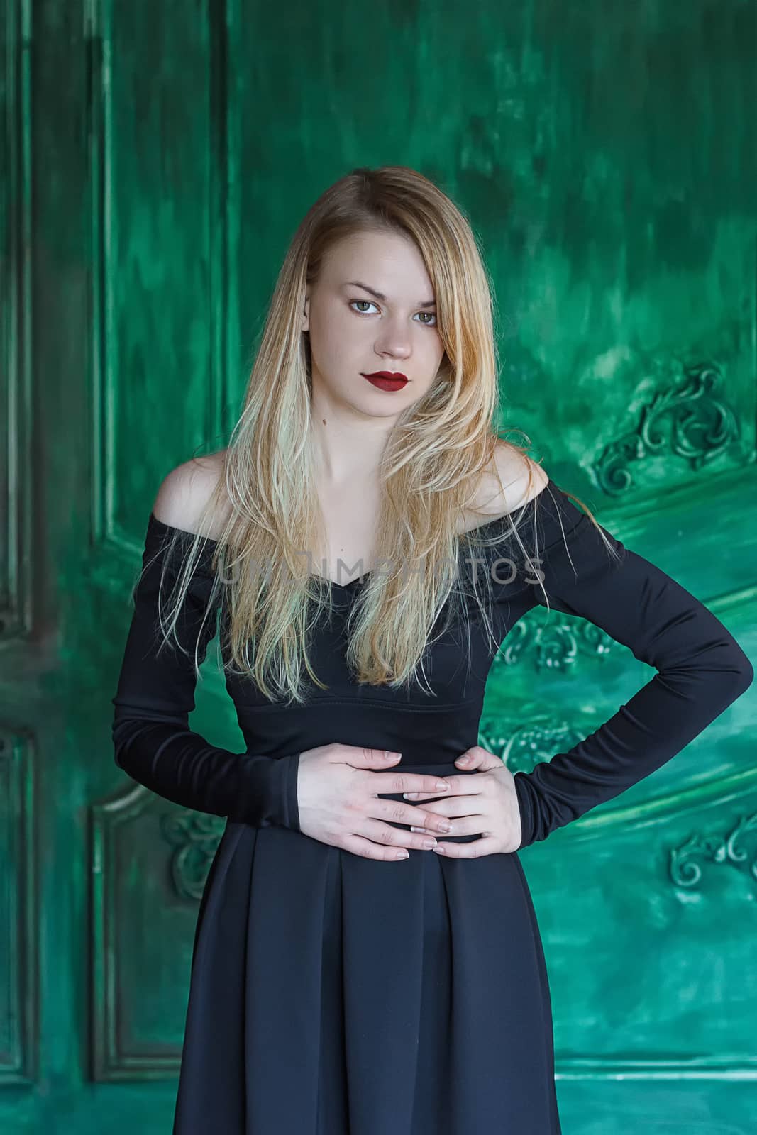 Elegant blonde in a black dress near grunge wall green