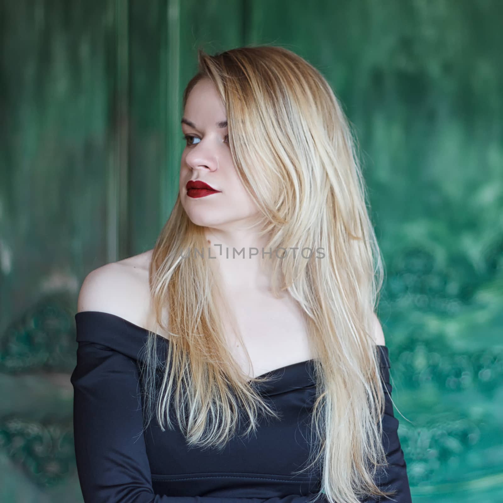 Elegant blonde in a black dress near grunge wall green