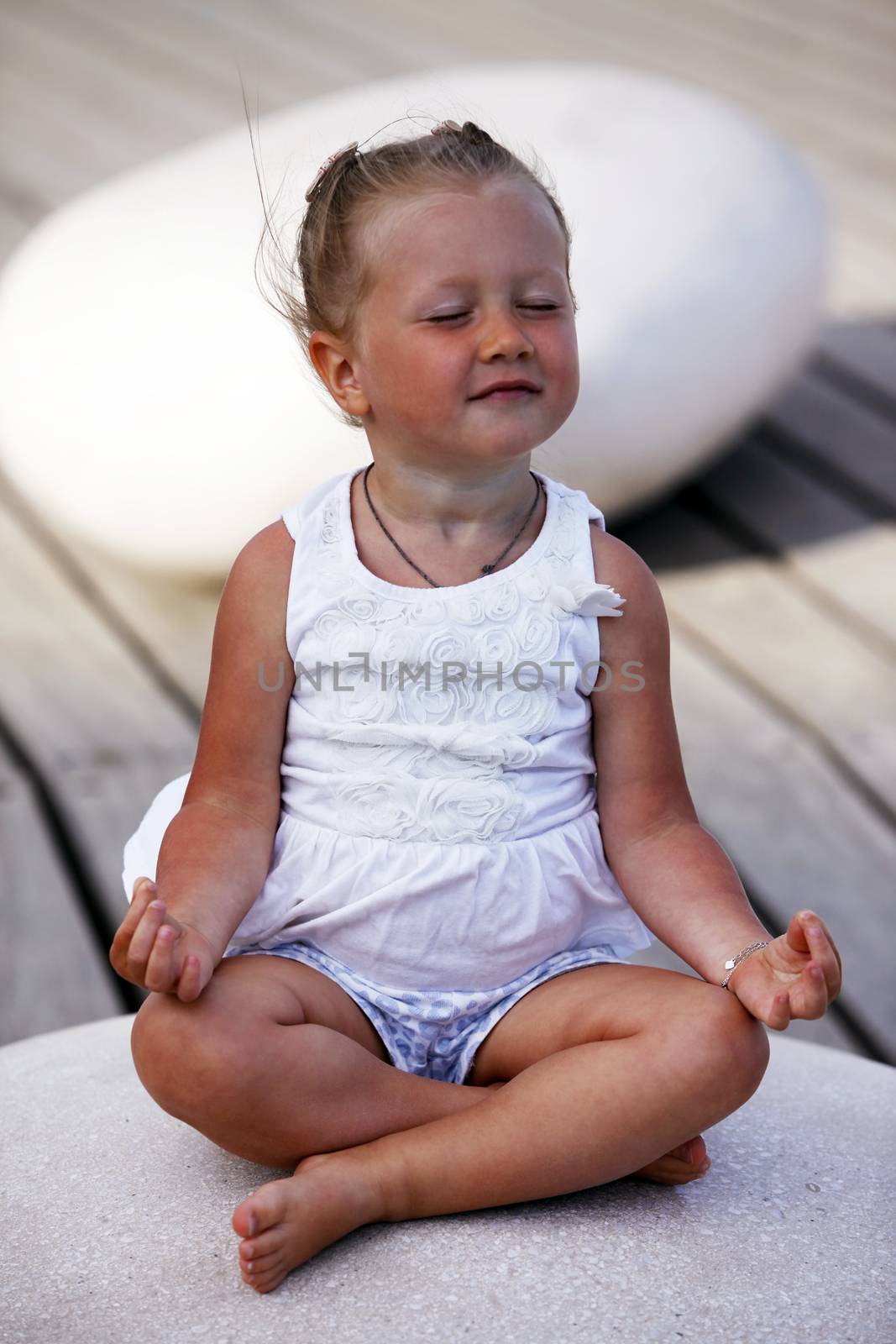 Adorable little girl doing yoga sitting on the big stone