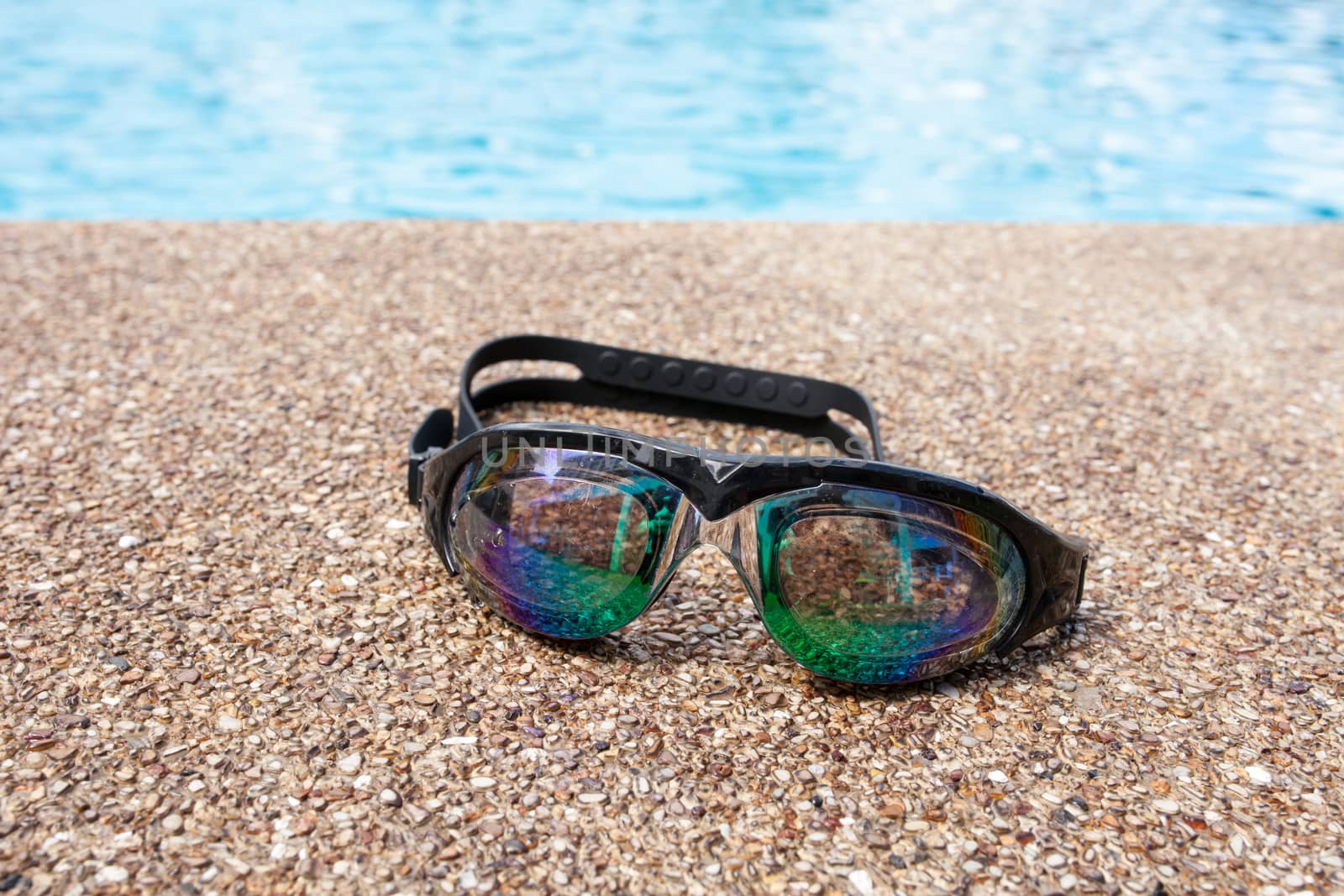 Glasses for swimming on a cement floor with small stone near swimming pool.