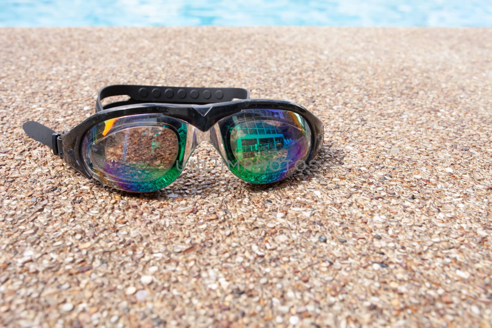 Glasses for swimming on a cement floor with small stone near swimming pool.