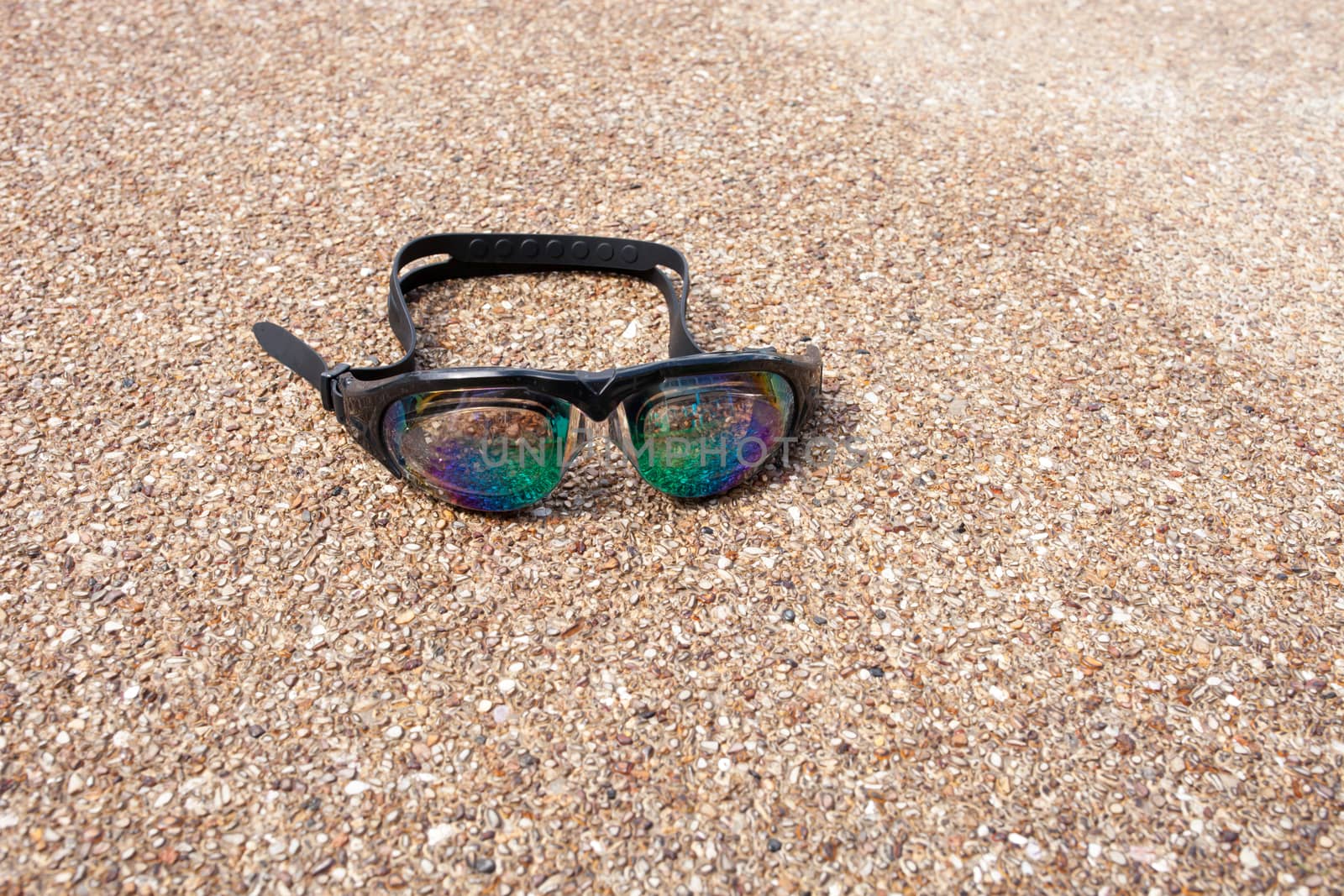 Glasses for swimming on a cement floor with small stone near swimming pool.