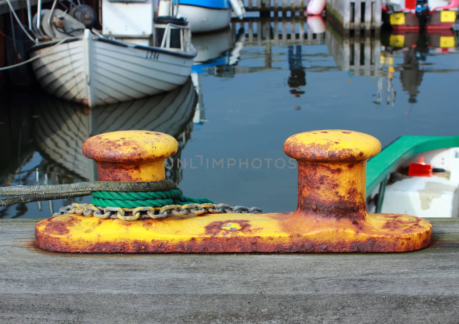 Metal bollard at small fishing harbor with ropes and chain