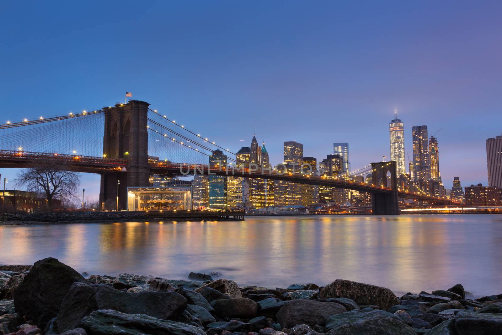 Brooklyn bridge and New York City Manhattan downtown skyline at dusk with skyscrapers illuminated over East River panorama. 