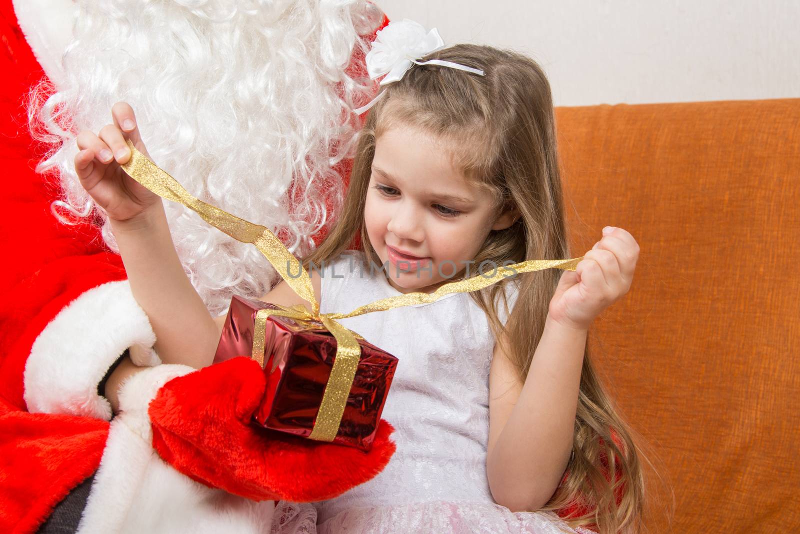 Girl unleashes a red ribbon gift in the hands of Santa Claus