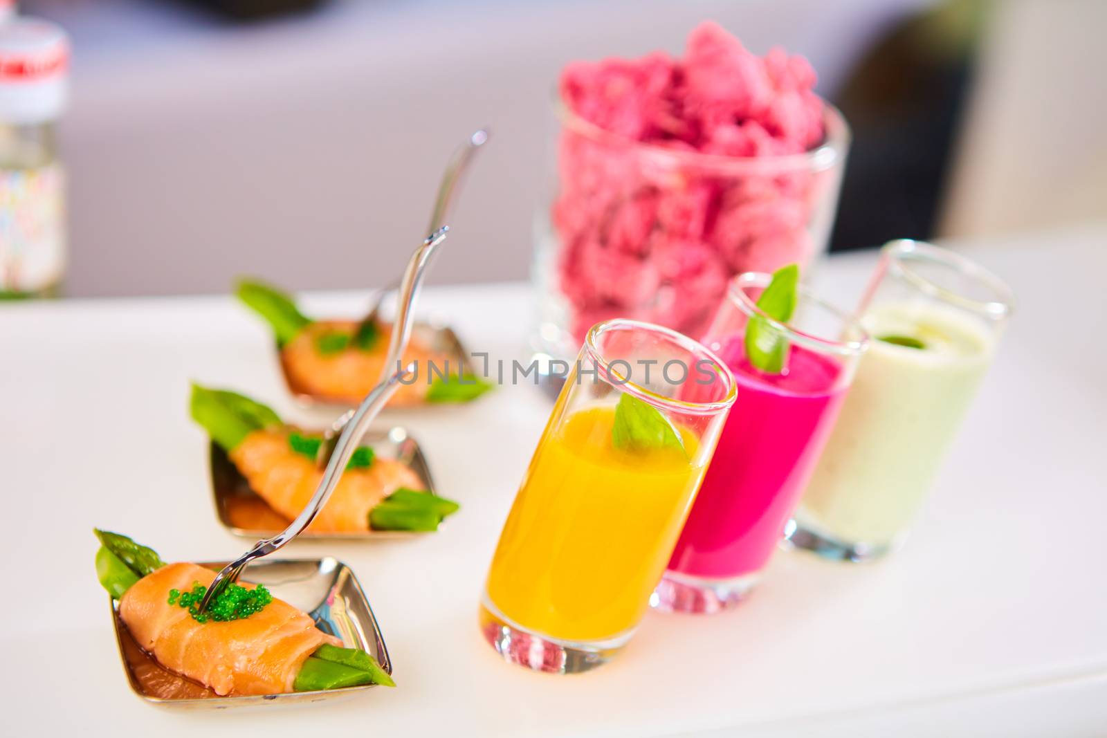 Appetizer plate of sauteed asparagus wrapped in thin slices of smoked salmon and different vegetable juice . Closeup with selective focus and shallow depth of field.