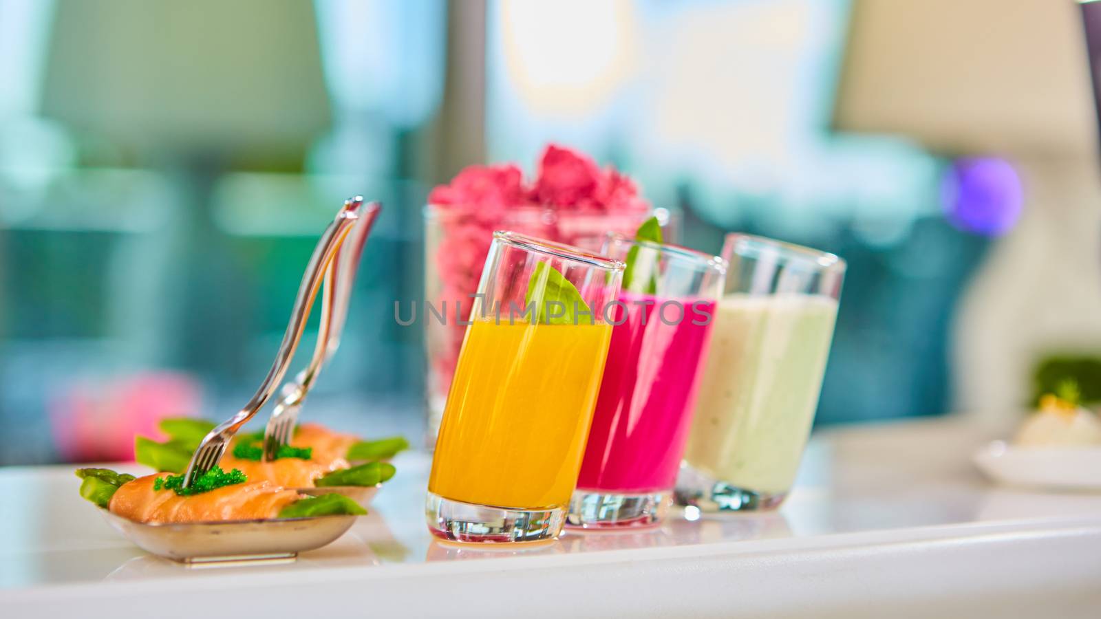Appetizer plate of sauteed asparagus wrapped in thin slices of smoked salmon and different vegetable juice . Closeup with selective focus and shallow depth of field.