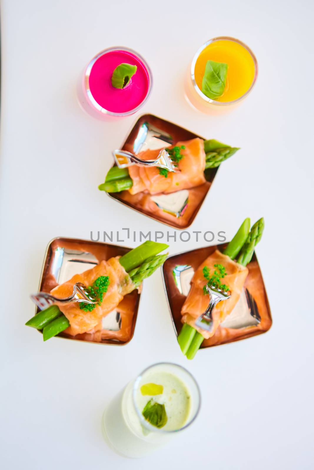 Appetizer plate of sauteed asparagus wrapped in thin slices of smoked salmon and different vegetable juice . Closeup with selective focus and shallow depth of field.