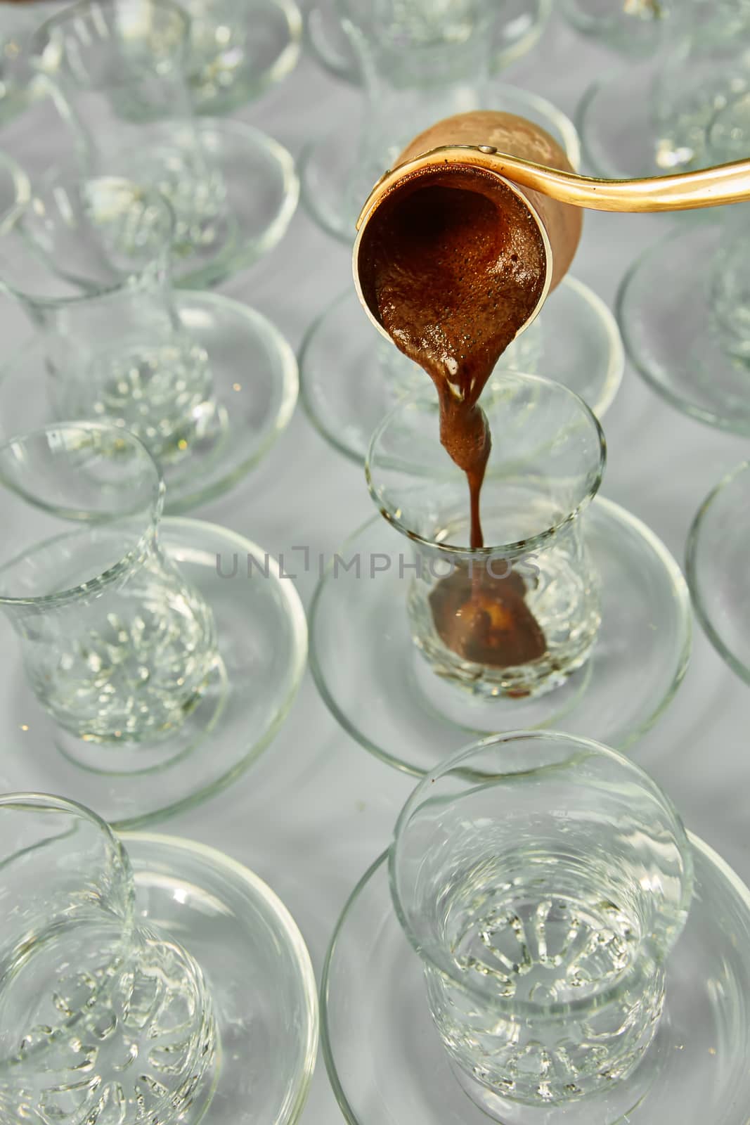 Pouring turkish coffee into traditional embossed glass cup.