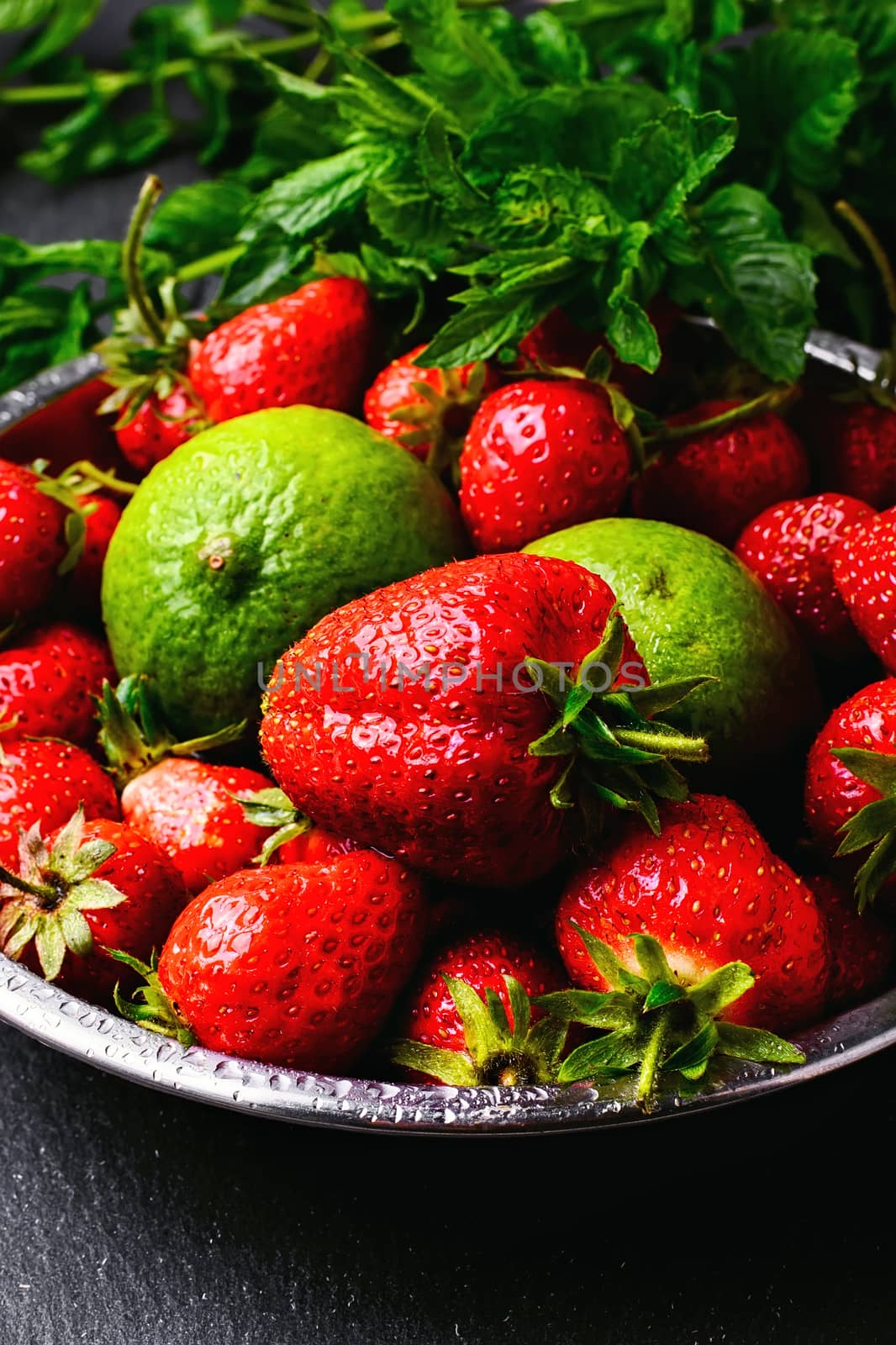 iron plate with ripe strawberry fruit and lime on a dark background