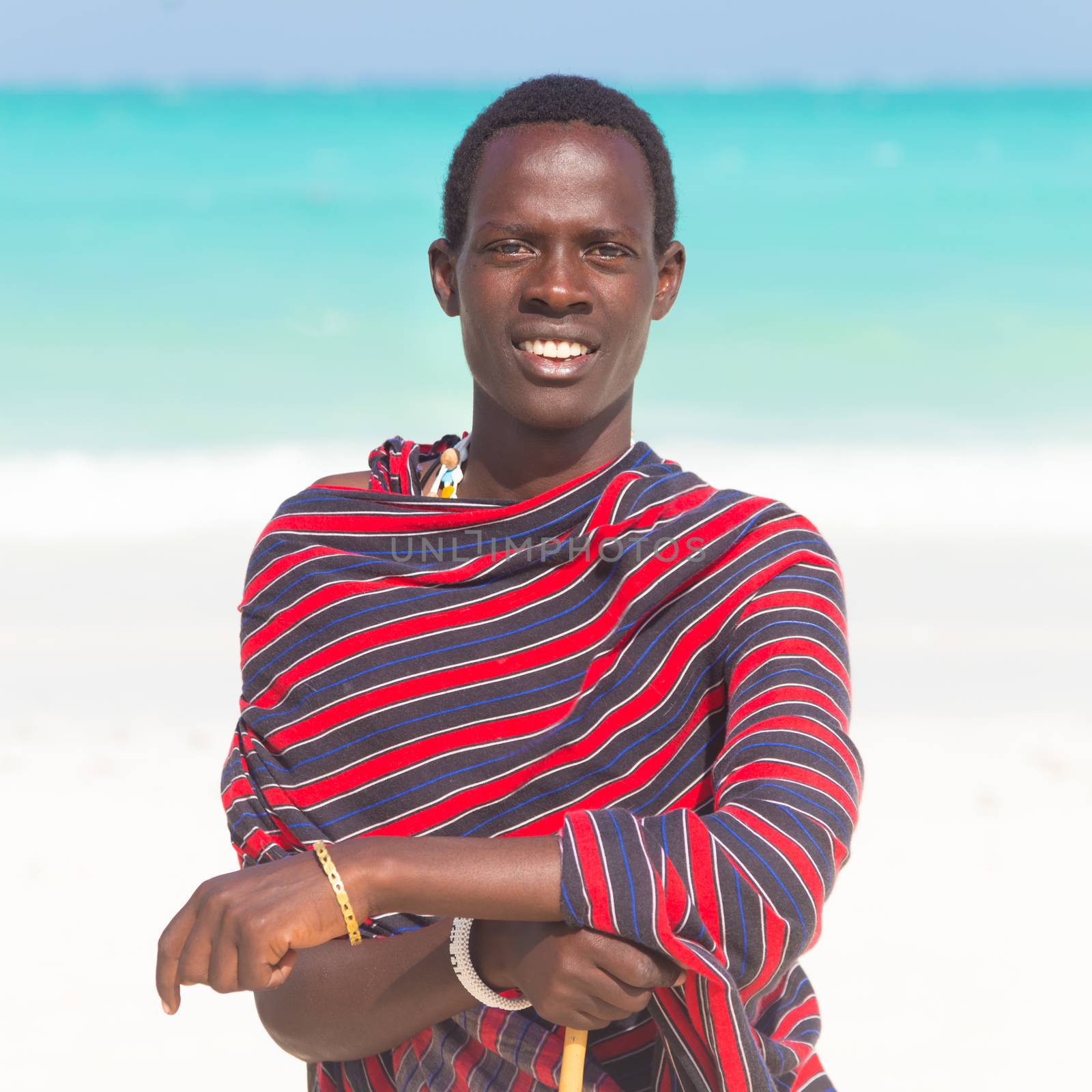 Traditonaly dressed black man on the beach. Maasai warrior on picture perfect tropical sandy beach on Zanzibar, Tanzania, East Africa.