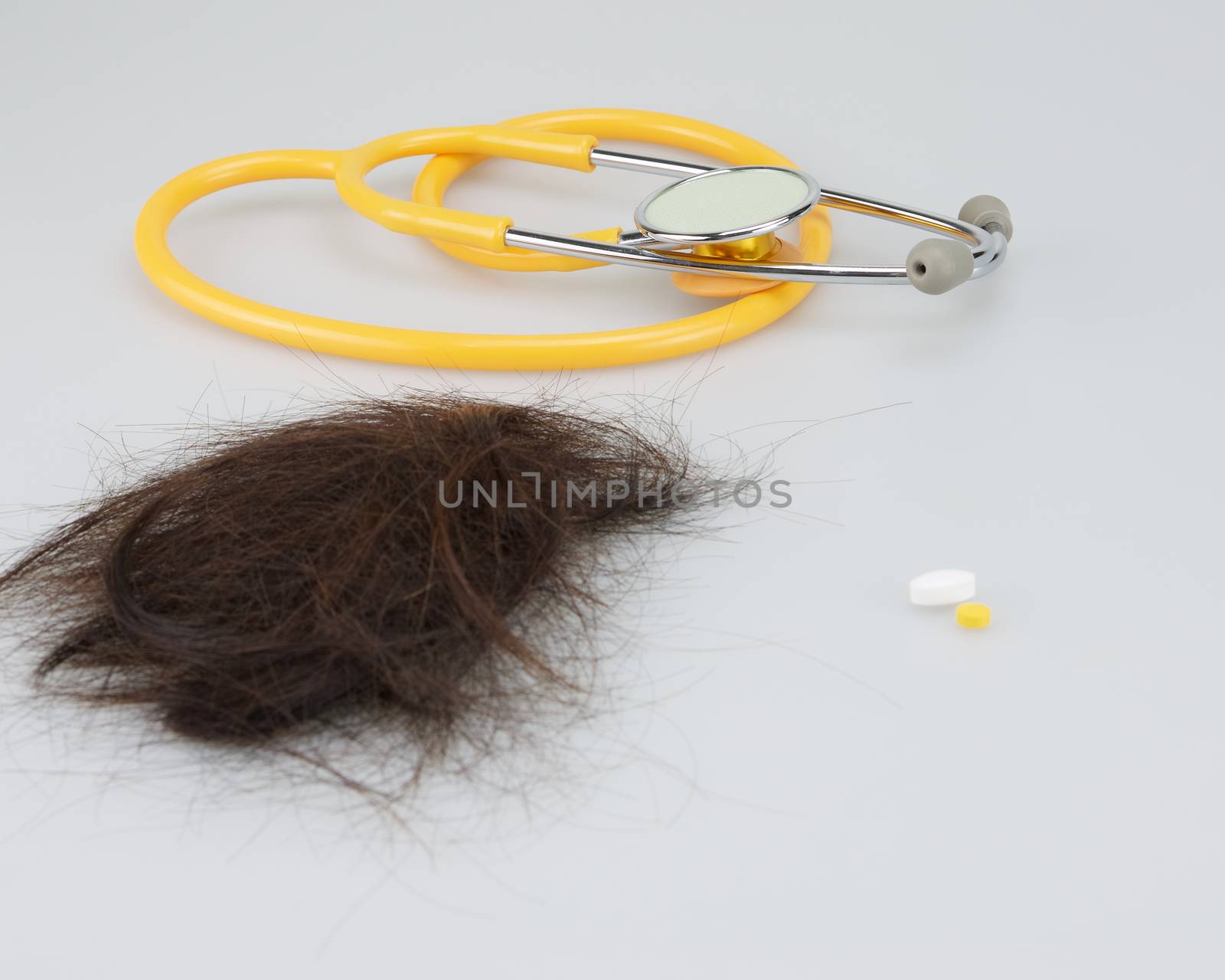 Brown lost hair with pill of medicine and stethoscope.