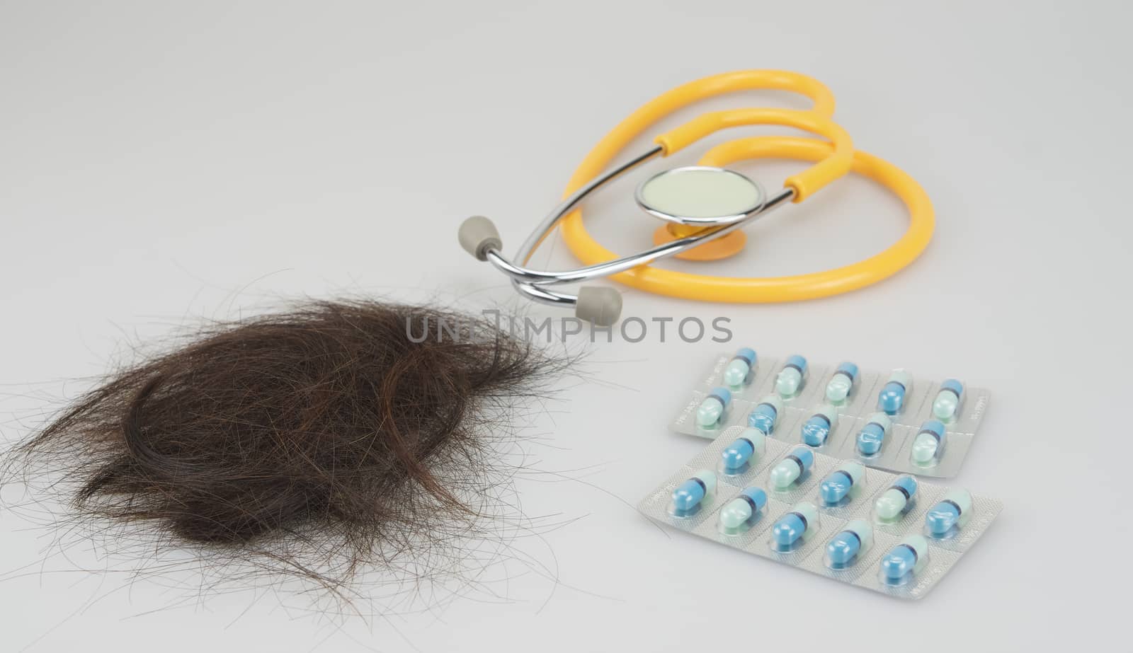 Brown lost hair with stethoscope and medicine placed on white background.