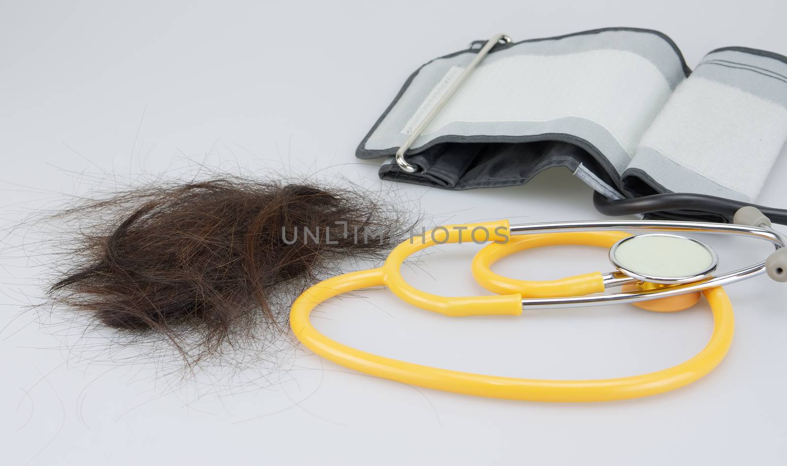 Brown lost hair with stethoscope and sphygmomanometer on white background.