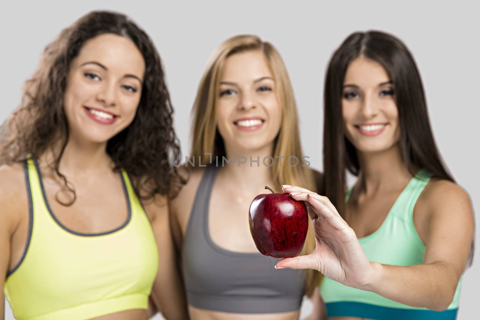 Portrait of three beautiful and athletic girls holding a red apple