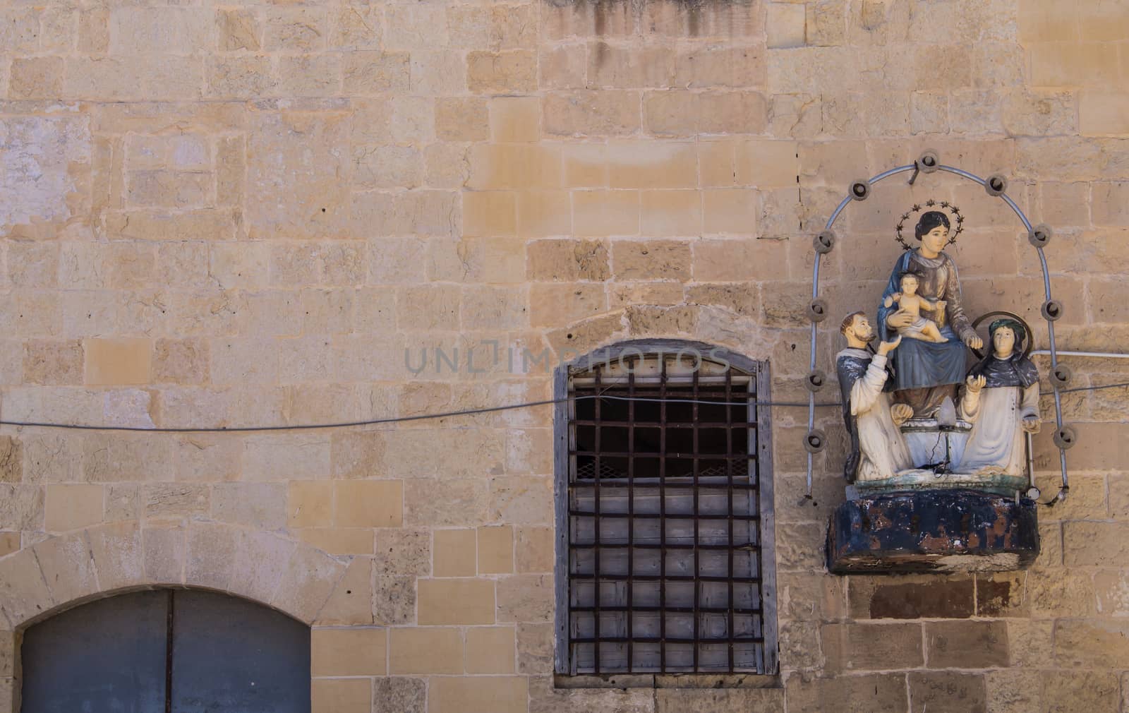 Building made of stone bricks with a window with grille and a saint statue. Capital of island Malta, Valletta.