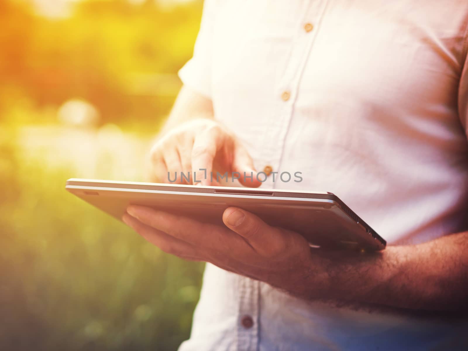Smart casual man with digital tablet outdoors, close up. Sunkissed effect with sunflares. Modern remote work concept.