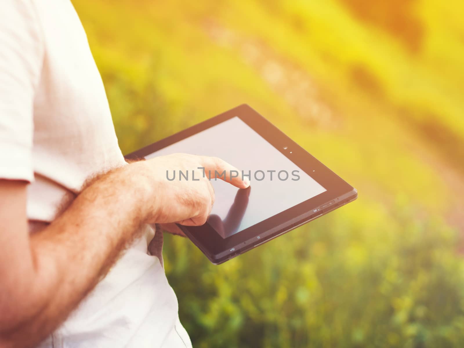 Smart casual man with digital tablet outdoors, close up. Focus on finger. Sunkissed effect with sunflares. Modern remote work concept.