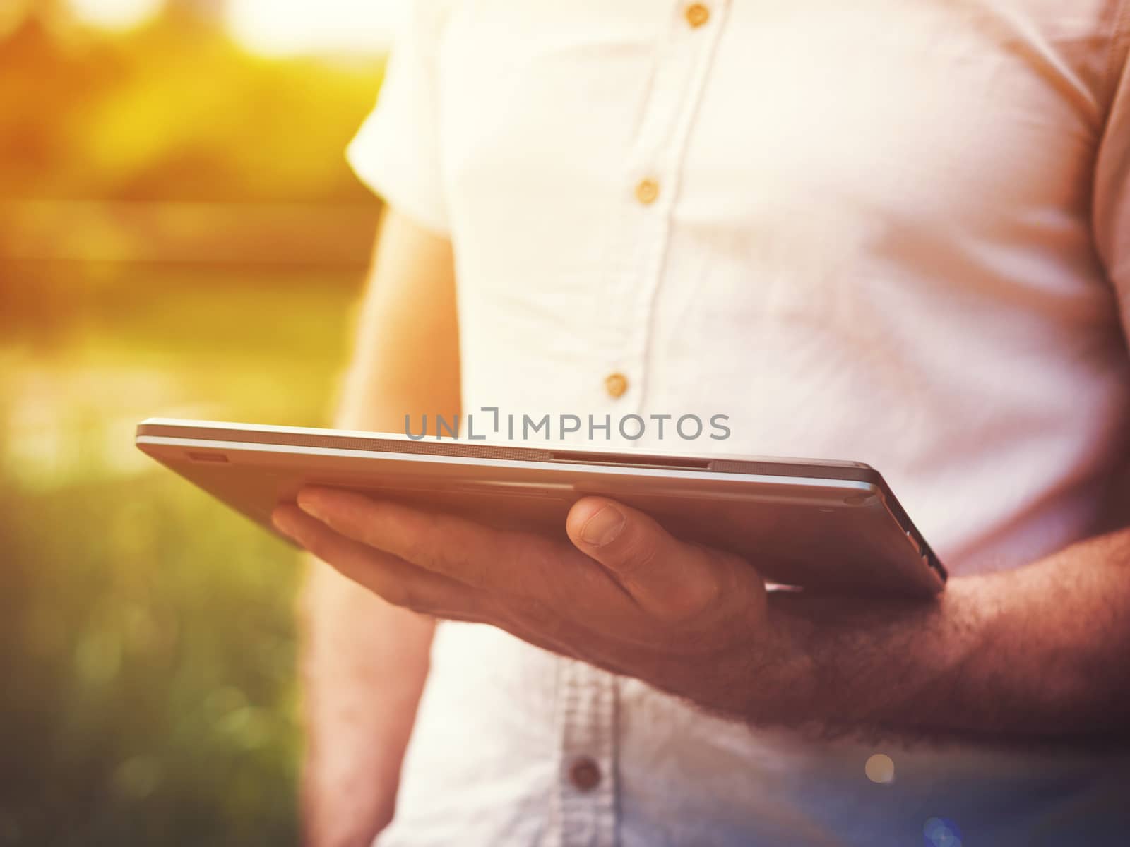 Smart casual man reading digital tablet outdoors. Sunkissed effect with sunflares. Modern remote work concept.