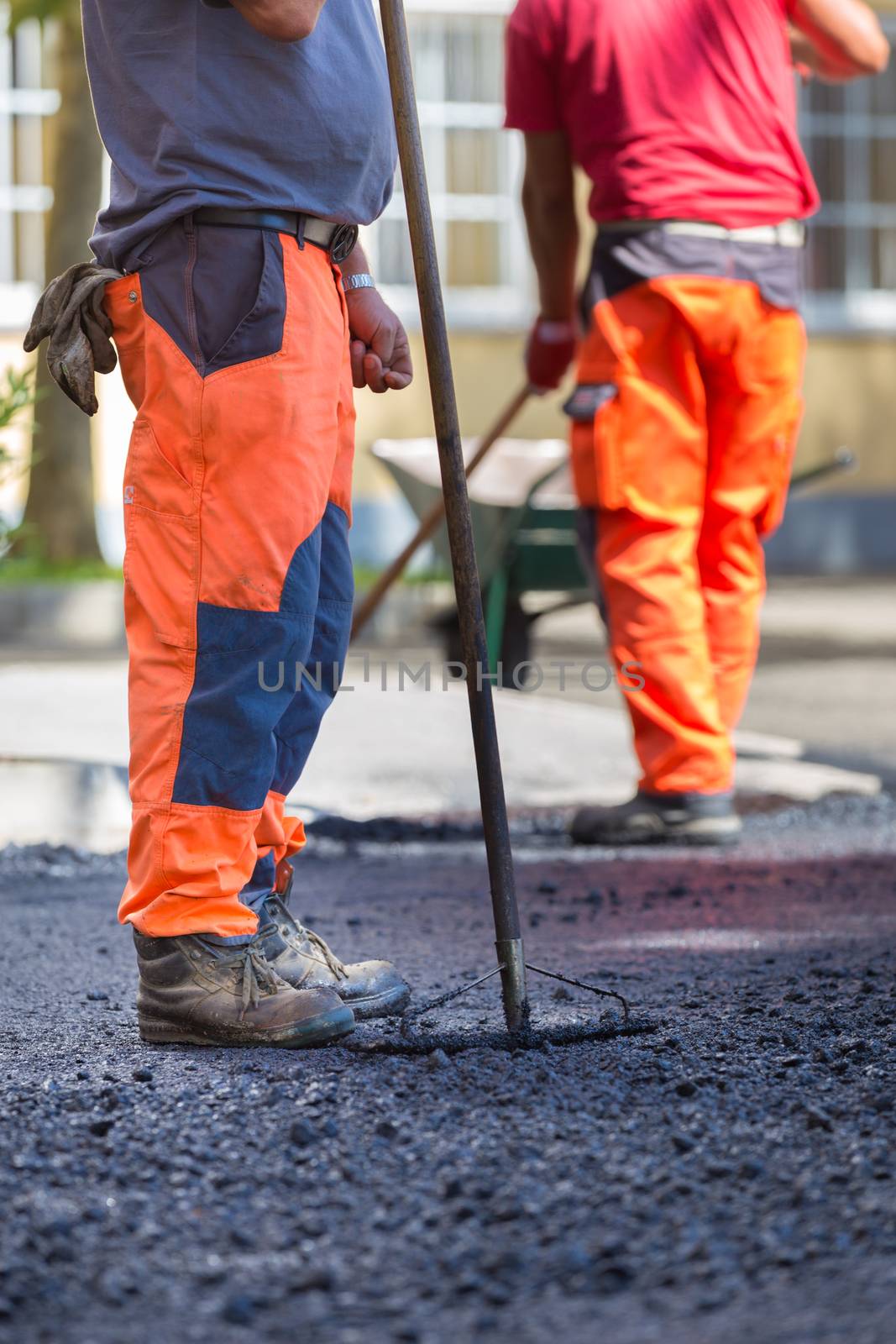 Construction workers during asphalting road works wearing coveralls. Manual labor on construction site.
