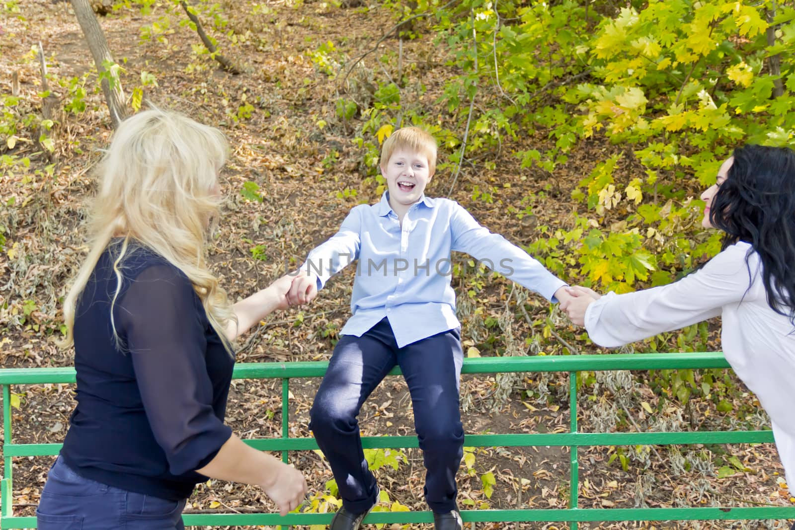 Two women pulling the boy to walk in autumn park