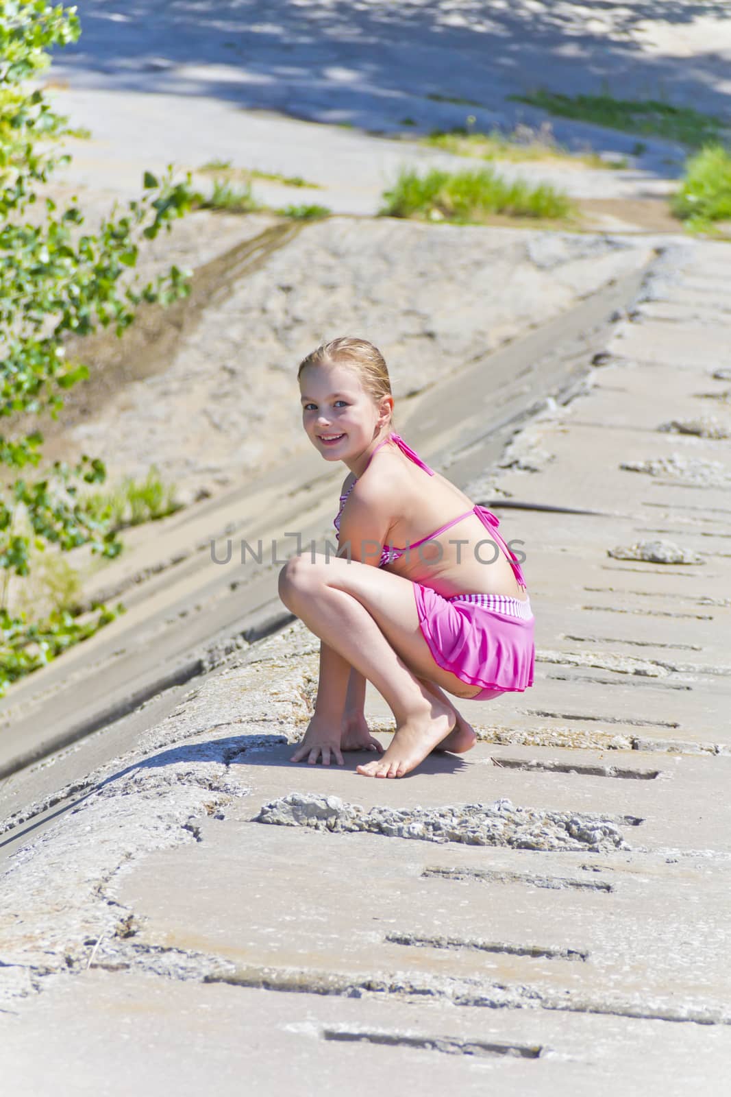 Cute jumping girl in pink swimsuit on the riverbank